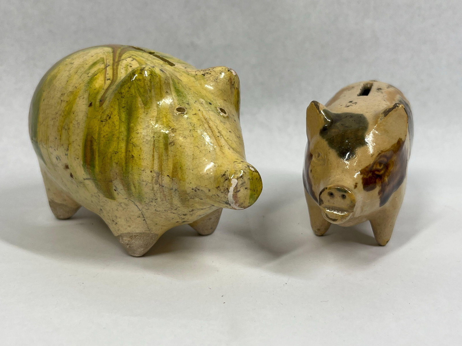 Pair Amer. Folk Art Pottery Piggy Banks: 5in ea. This lot consists of two hand-formed earthenware figural piggy banks. The larger bank is designed with an elongated snout, small pointed ears, and four tapered legs. It features a multi-color 
