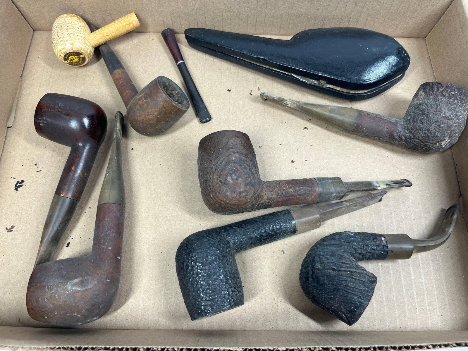 Missouri Meerschaum & Cellini Pipes: An assortment of vintage smoking pipes and accessories including various briar and corn cob examples. The collection features a Missouri Meerschaum corn cob pipe with its original paper base label