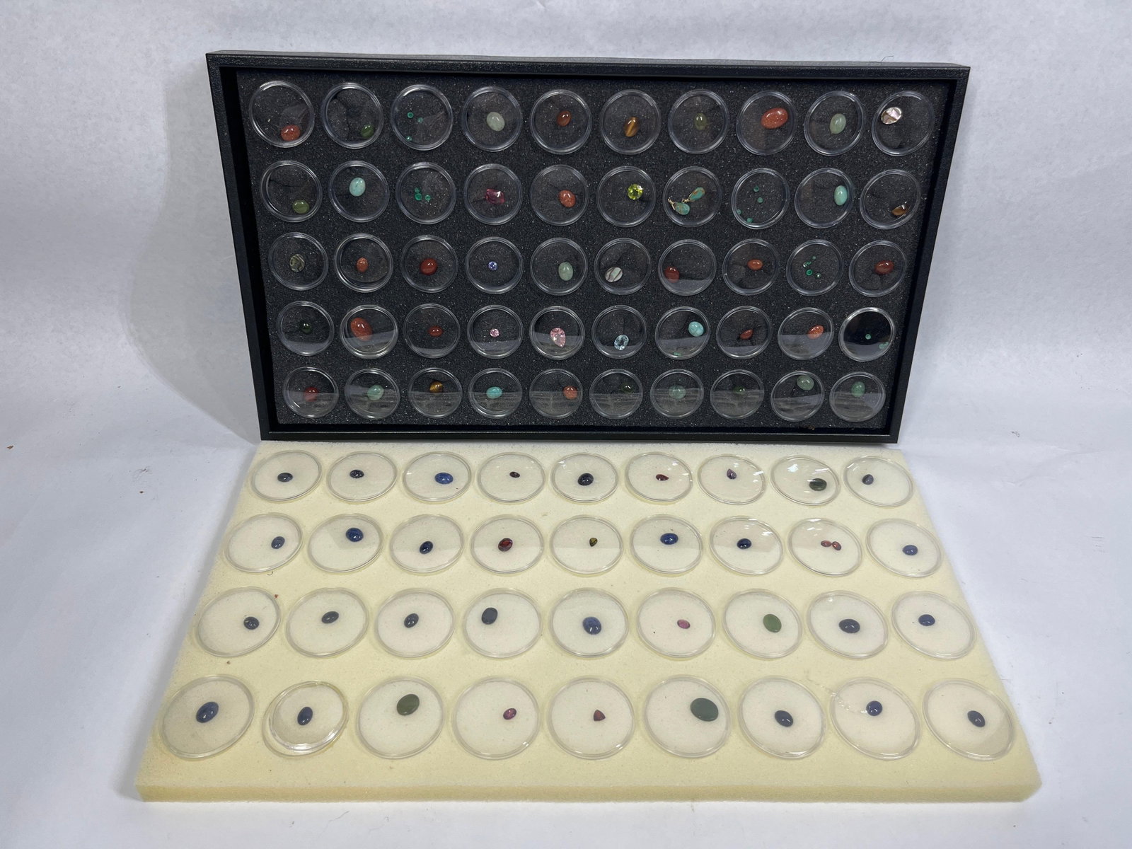 Loose Gemstones & Mineral Specimens: A comprehensive collection of loose gemstones and mineral specimens presented in two foam-lined display trays. The collection comprises approximately one hundred clear plastic circular gem jars. The