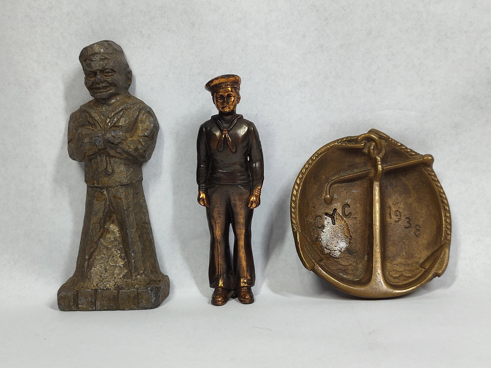 3 Nautical and Navy Metal Figures & Anchor Dish: A lot of three nautical-themed metal objects comprising two sailor figurines and a commemorative dish. The first figurine is a heavy cast metal stylized sailor depicted in a traditional uniform with