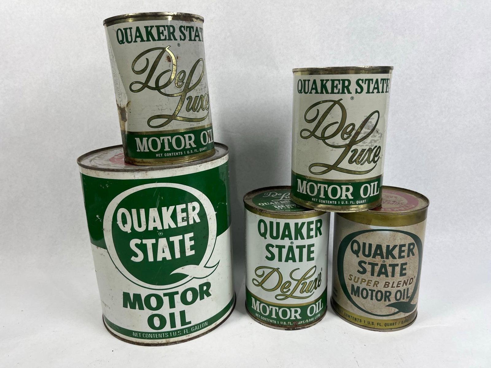 Set 5 Quaker State Motor Oil Cans: A collection of five vintage Quaker State motor oil cans constructed of lithographed tin. This group consists of one 1-gallon can and four 1-quart cans. The 1-gallon can features a green and white