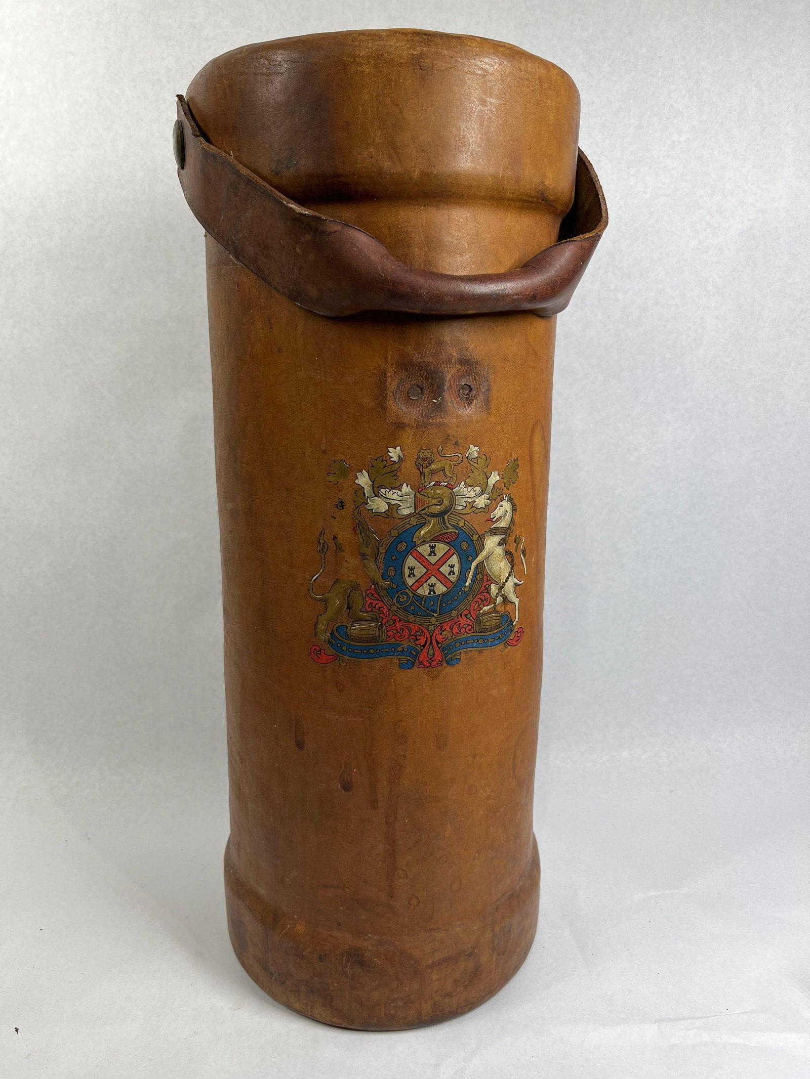 English Leather Heraldic Umbrella Stand: 20in This is a tall, cylindrical stand crafted from thick, heavy-gauge brown leather. The item is modeled after traditional English leather blackjacks but functions as a decorative receptacle for