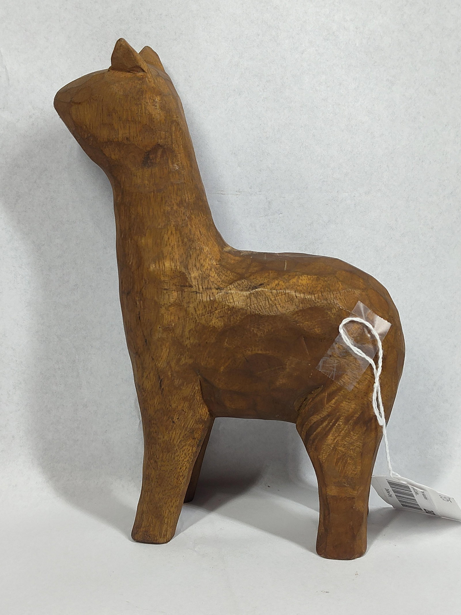 Folk Art Carved Wood Llama Figurine: 9.5x6x2 This hand-carved wooden figurine depicts a stylized llama or alpaca in a rustic folk art manner. The piece is constructed from a single block of medium-toned wood, featuring prominent faceted