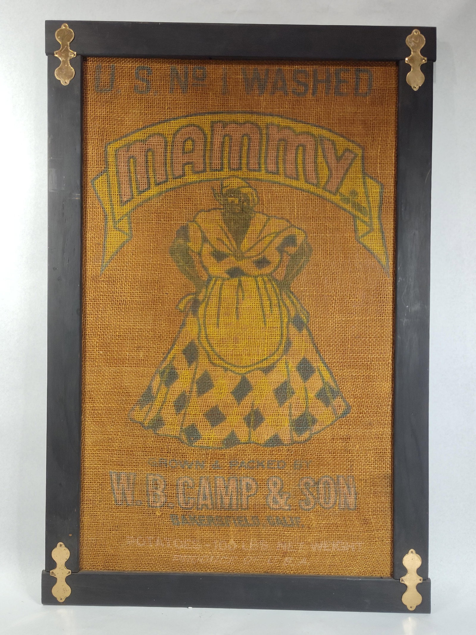 Mammy Brand Burlap Potato Sack, Framed: 23x34 A framed vintage burlap advertising sack for Mammy brand potatoes. The central graphic features a caricature of a Black woman in a yellow and black diamond-patterned dress and yellow apron,
