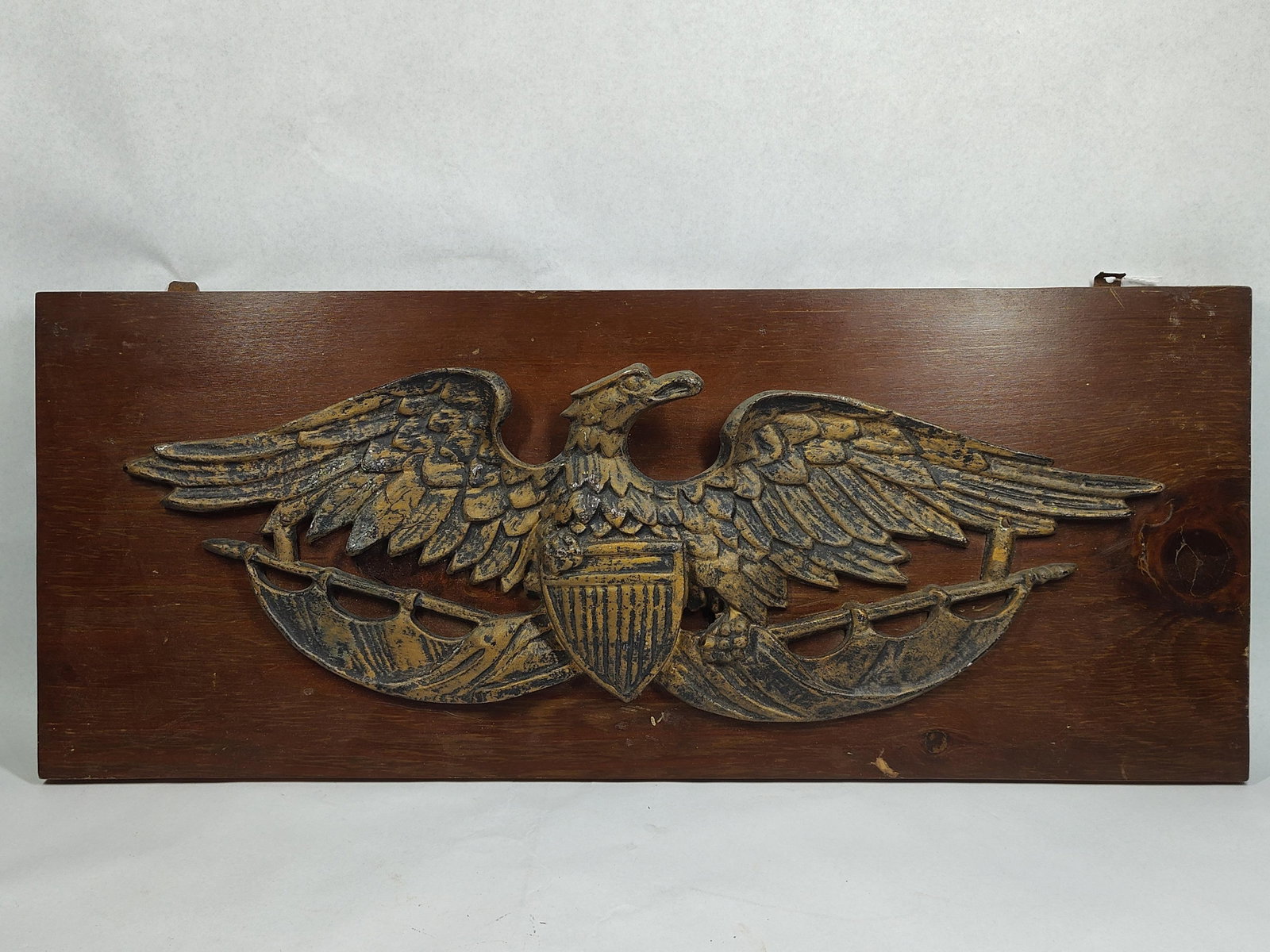 Federal Cast Aluminum Eagle Wall Plaque: 28x11 This wall plaque features a cast aluminum American eagle emblem mounted on a rectangular stained wood panel. The eagle is rendered in the Federal style, depicted with outstretched wings and its 