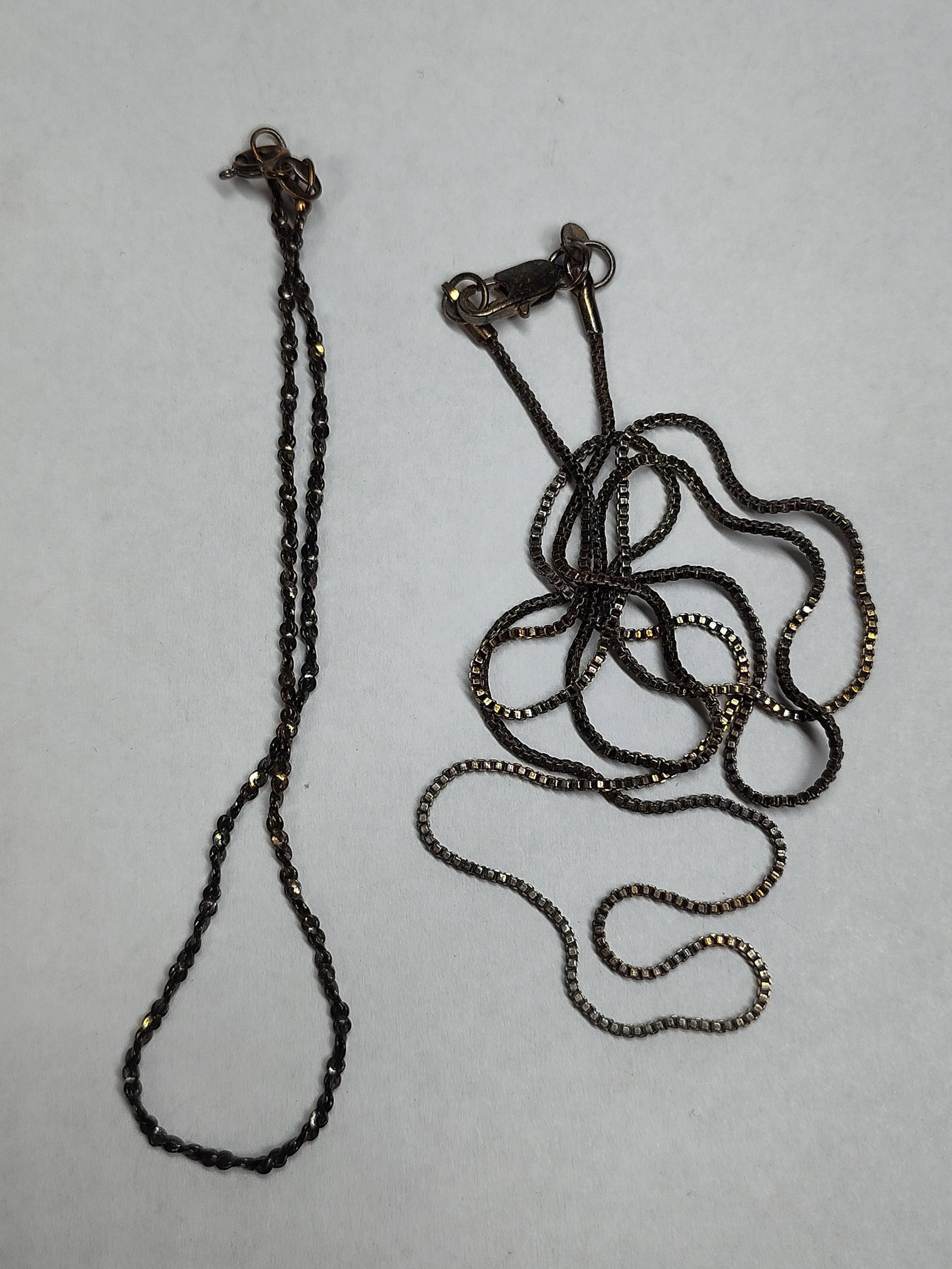Two Sterling Silver Necklace Chains: This lot consists of two sterling silver necklace chains in differing styles. The first chain is a fine rope or twisted link style and is secured with a spring ring clasp. The oval jump ring tag is ha
