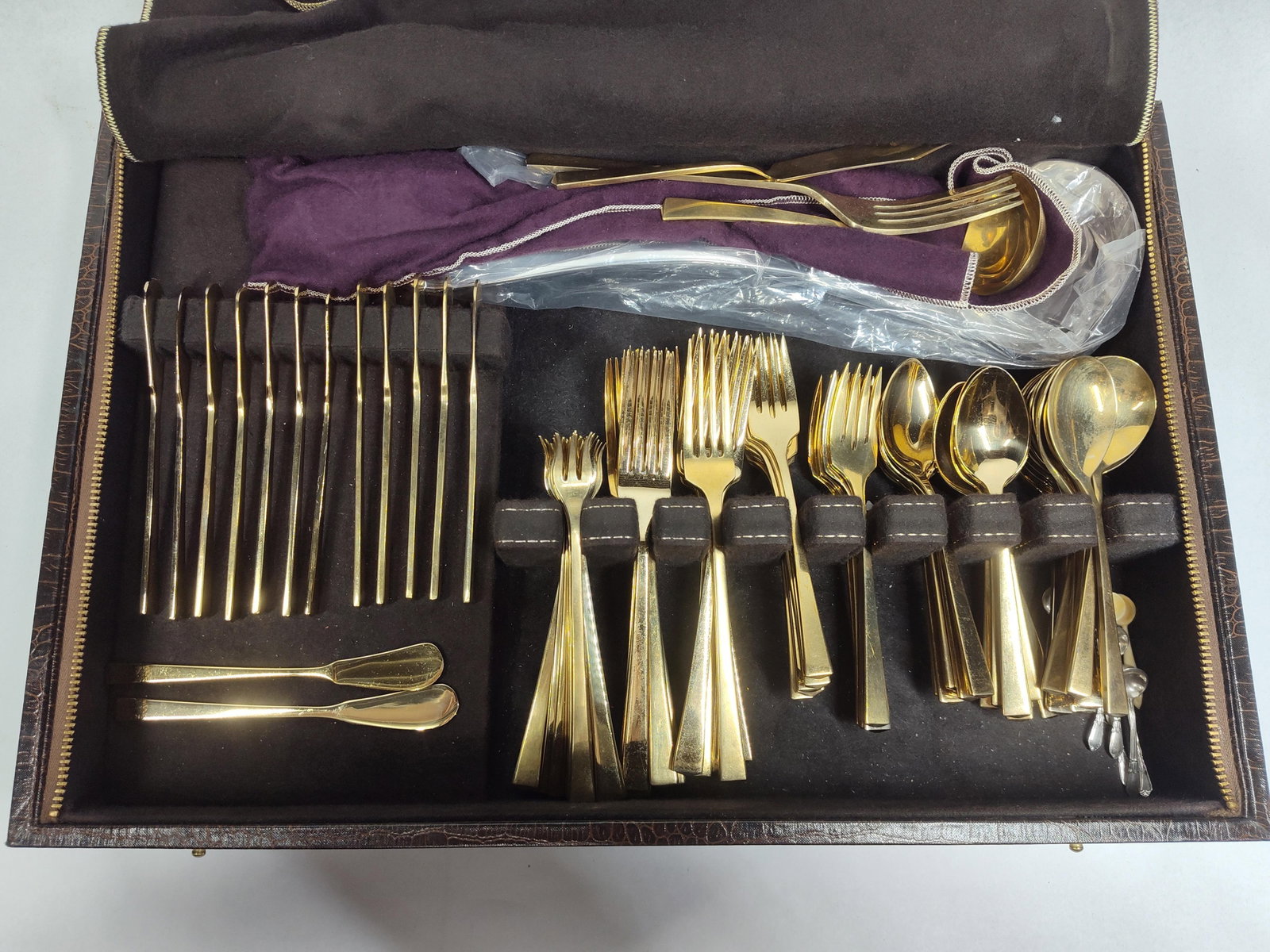 Dirilyte Gold Bronze Flatware & Servers: This collection features a service of gold-toned bronze flatware manufactured by Dirilyte. The handles are marked DIRILYTE and feature a mid-century modern style with tapered handles and square ends.