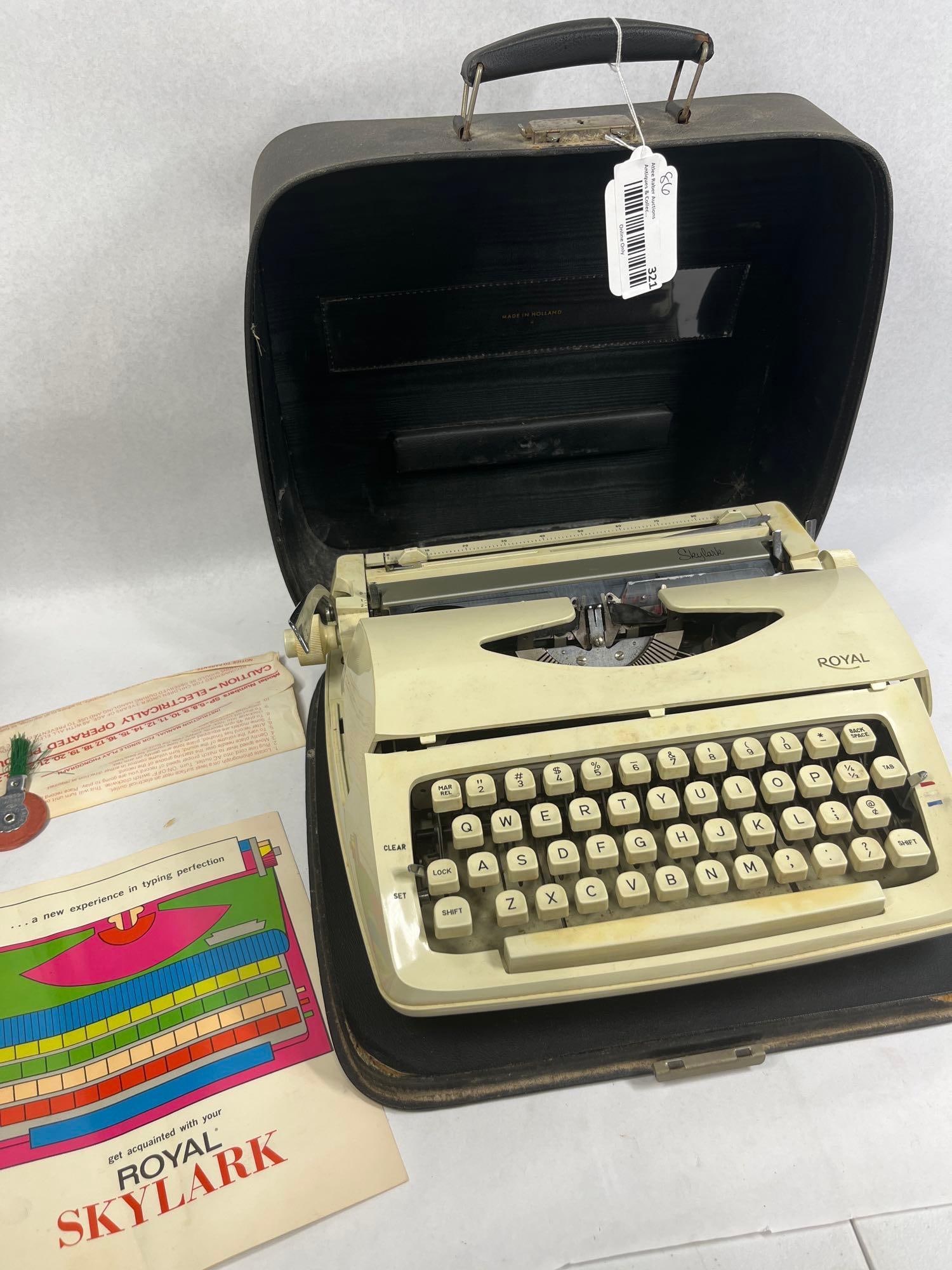 Royal Skylark Manual Typewriter w/ Case: A vintage Royal Skylark portable manual typewriter, manufactured in Holland. The machine features a cream-colored housing with a standard QWERTY keyboard layout. The maker mark Royal is located on
