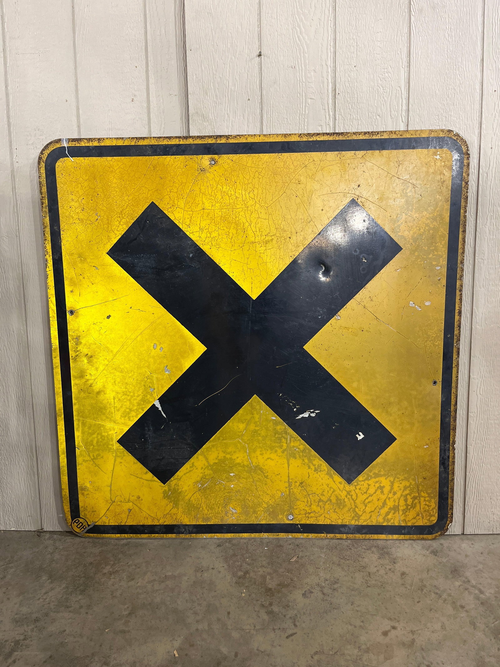 Painted Metal Crossroad Sign: 48x48 A vintage roadside hazard warning sign featuring a bold black crossbuck or X symbol centered on a bright yellow square field, enclosed by a black border. The sign is constructed from