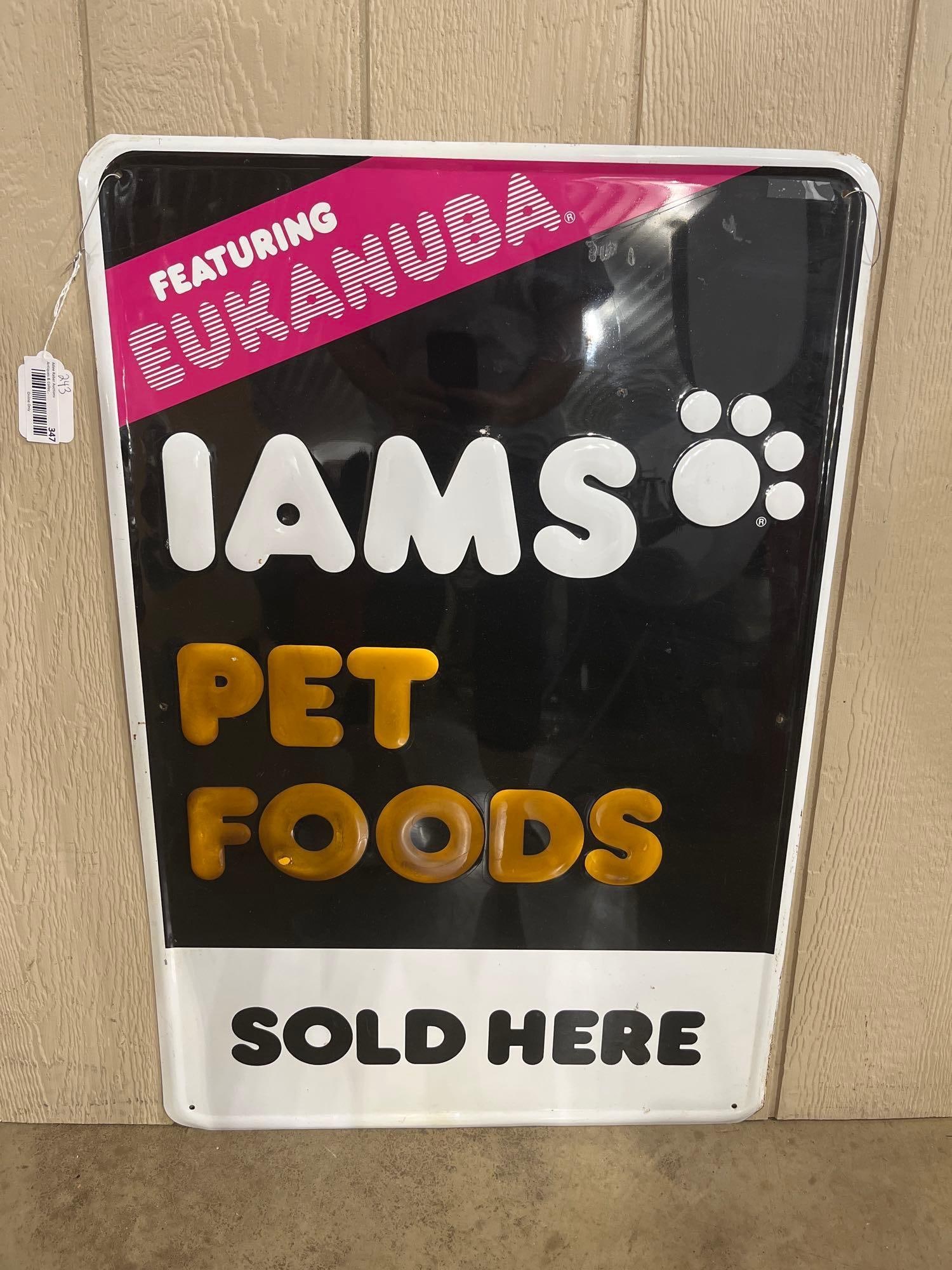 Iams & Eukanuba Embossed Metal Sign: 24x 36 This is a vertical rectangular retail advertising sign for Iams and Eukanuba pet foods. The sign is constructed of painted embossed metal with a multi-colored graphic design on a black field. A