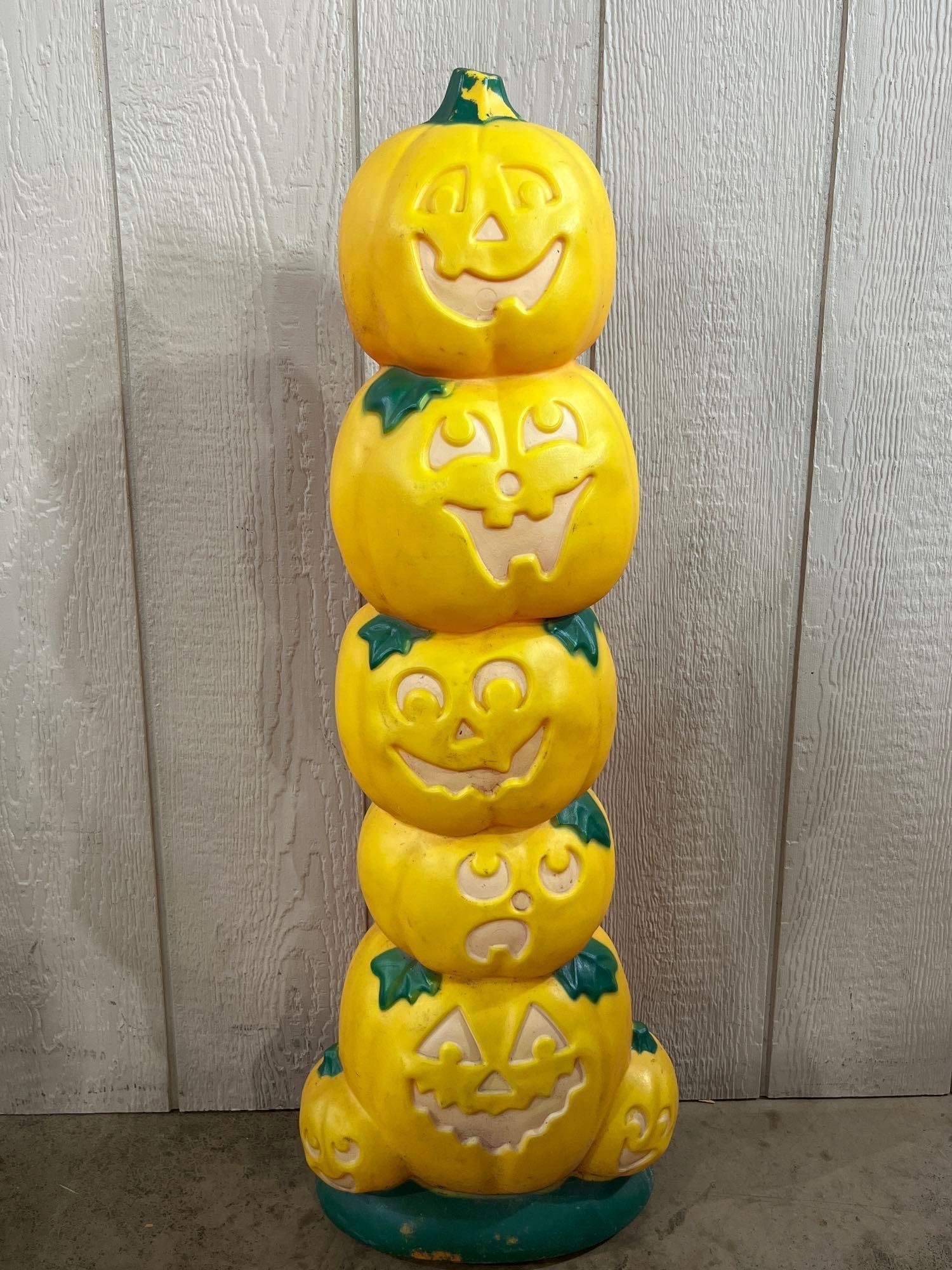 Sun Hill Style Jack-O-Lantern Blow Mold: 38in tall This is a vertical Halloween decoration featuring a stack of five jack-o-lantern pumpkins, each sculpted with a distinct facial expression. The central column is supported at the bottom by