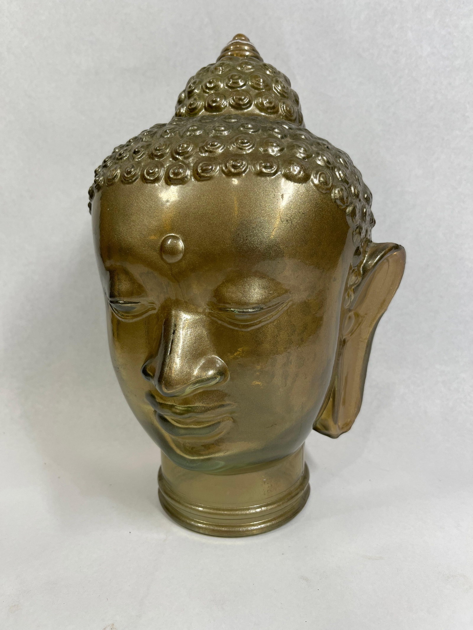 Gold Luster Glass Buddha Head Sculpture: This decorative sculptural bust represents a Buddha head, designed in a style influenced by Southeast Asian religious traditions, particularly Thai and Khmer sculpture. The object is constructed from
