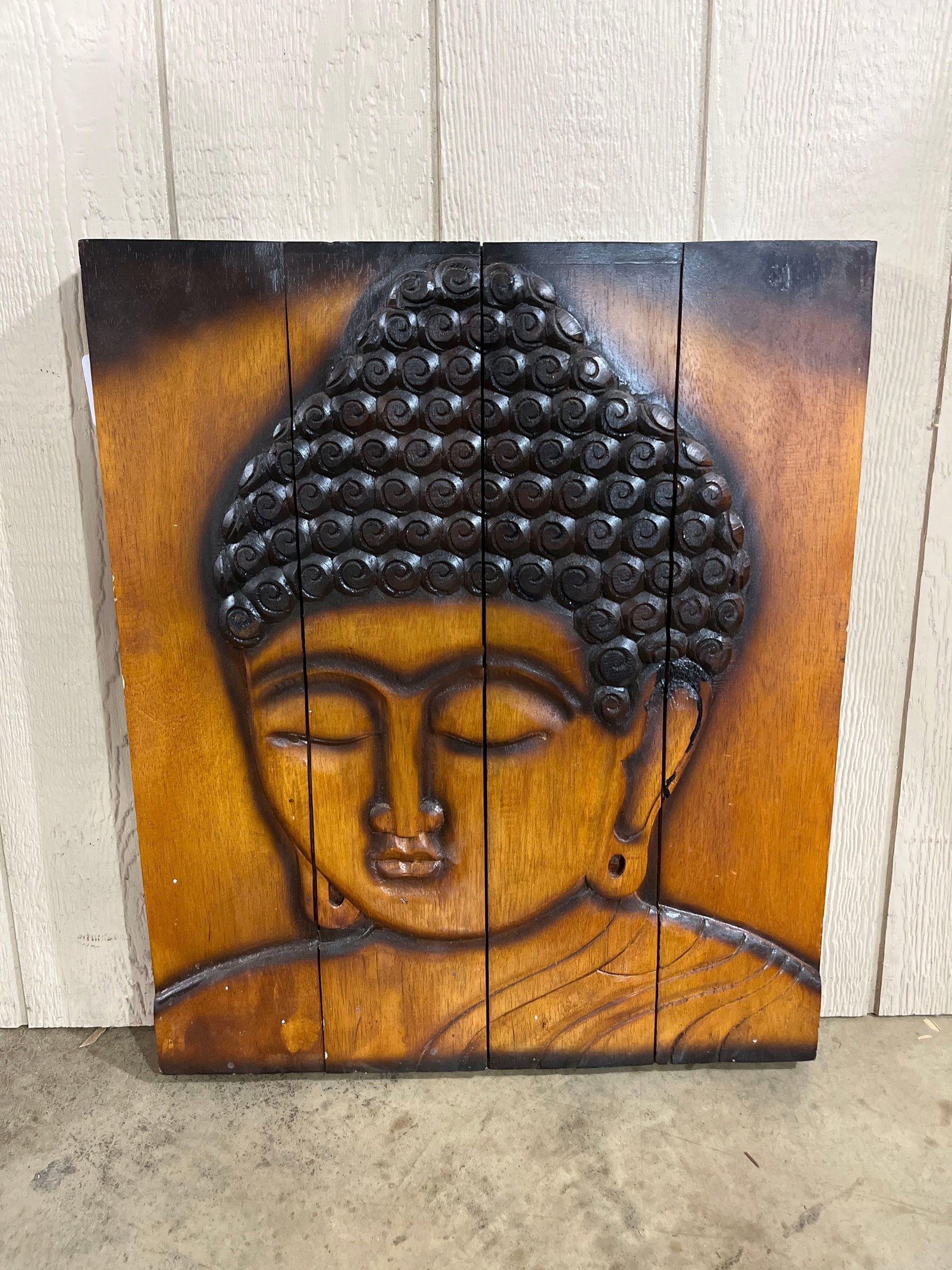 World Market Carved Wood Buddha Plaque: 28x23 This decorative wall plaque is attributed to World Market and features a high-relief carving of a Buddha head. The piece is constructed from four vertical wooden planks joined together and