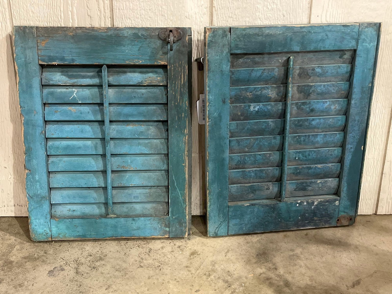 Pair Teal Louvered Wood Shutters: 18x14 This lot features a pair of louvered wooden window shutters characterized by a heavily weathered teal blue-green painted finish. The shutters are constructed with a rectangular wood frame