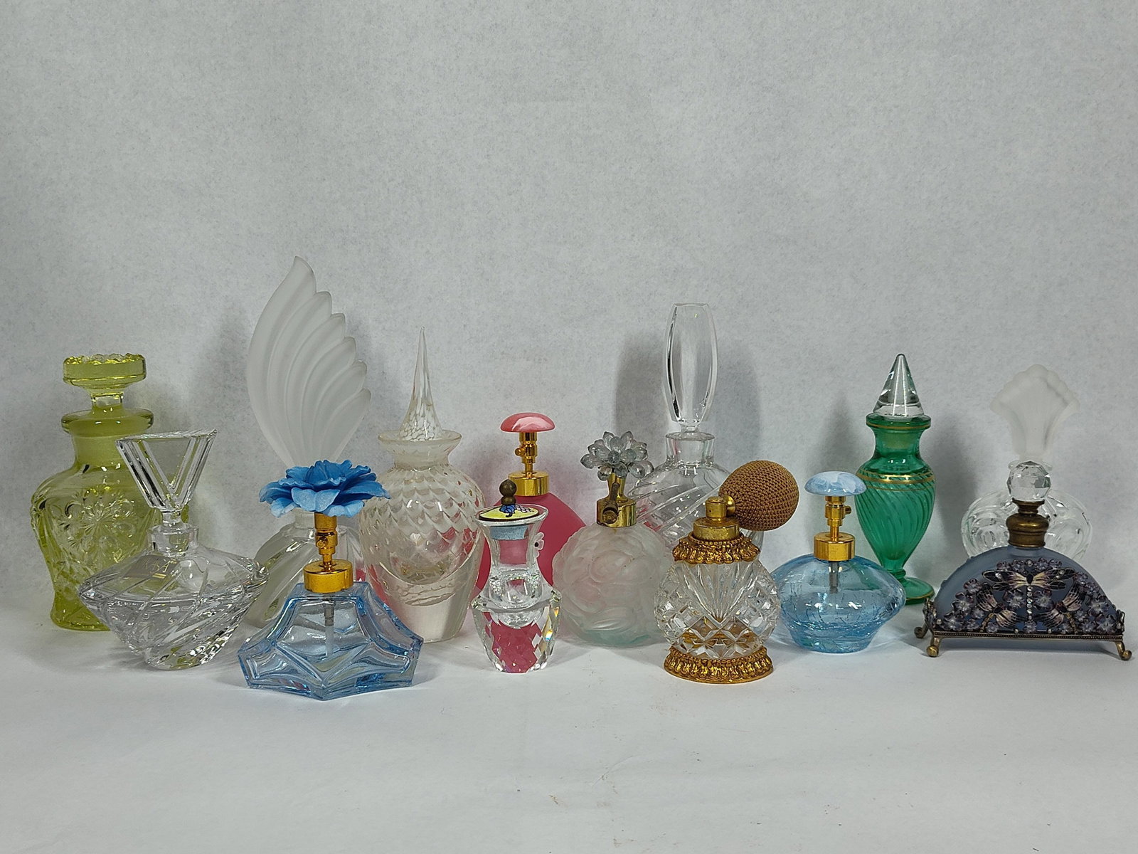 14 Glass Perfume Bottles & Atomizers: This assortment of fourteen decorative glass perfume bottles and atomizers displays a variety of glassmaking techniques and styles. A featured piece is a clear cut crystal bottle with a twisted