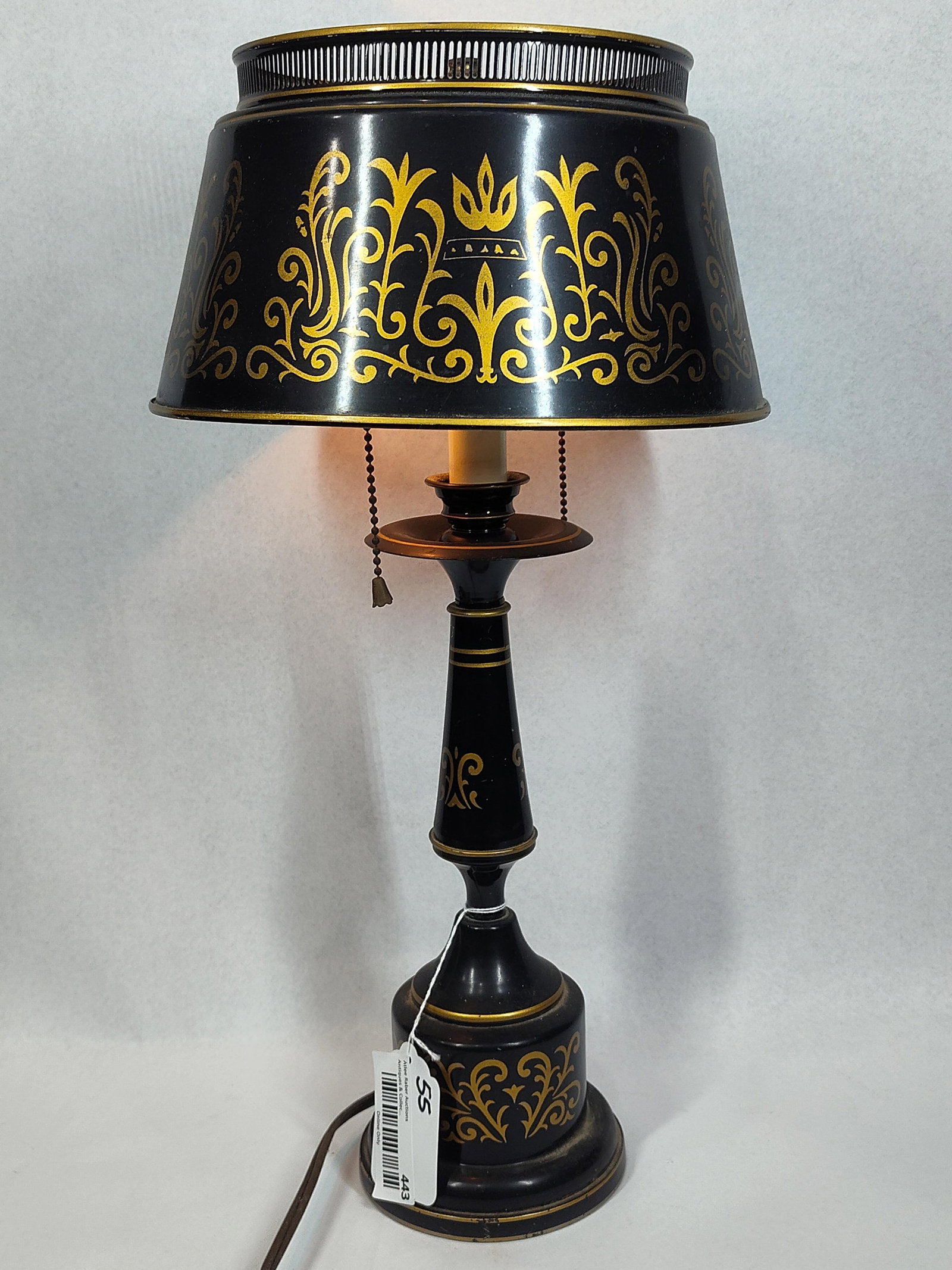 Mid-C. Black & Gold Tole Bouillotte: 20in A mid-century table lamp in the bouillotte style, constructed from painted metal with a matte black finish. The lamp and its matching flared metal shade are decorated with gold-toned stenciled