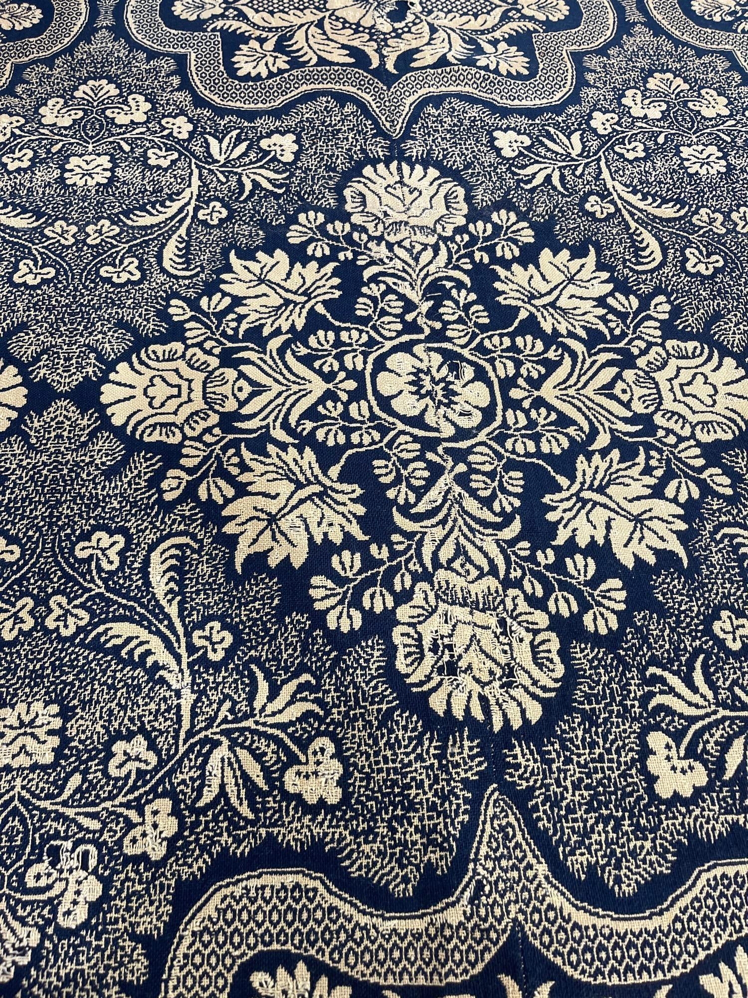 19th C. American Indigo & Cream: 75x76 An antique American jacquard coverlet woven in a two-color palette of indigo blue and cream. The textile features a repeating symmetrical pattern centered around large floral medallions,