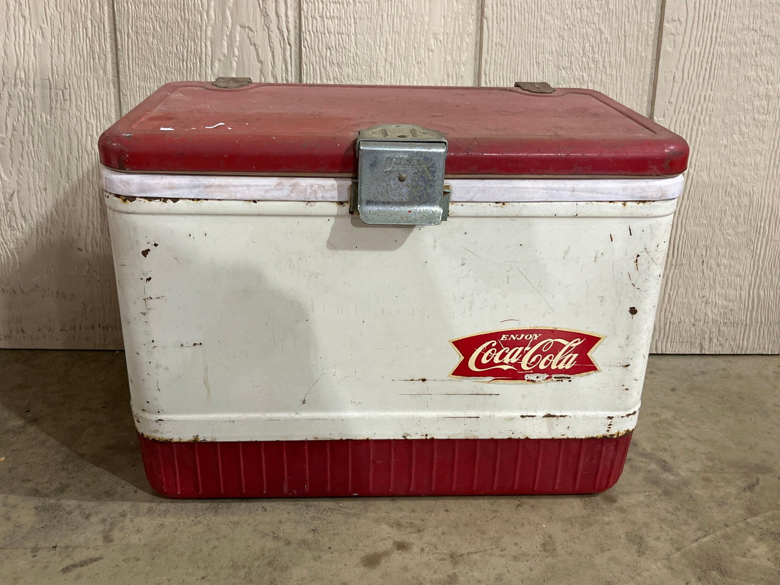Poloron Coca-Cola Metal Fishtail Cooler: A vintage Coca-Cola metal ice chest manufactured by Poloron, featuring the brands fishtail logo used between 1958 and 1965. The cooler is constructed with a red painted metal lid and a red corrugated 