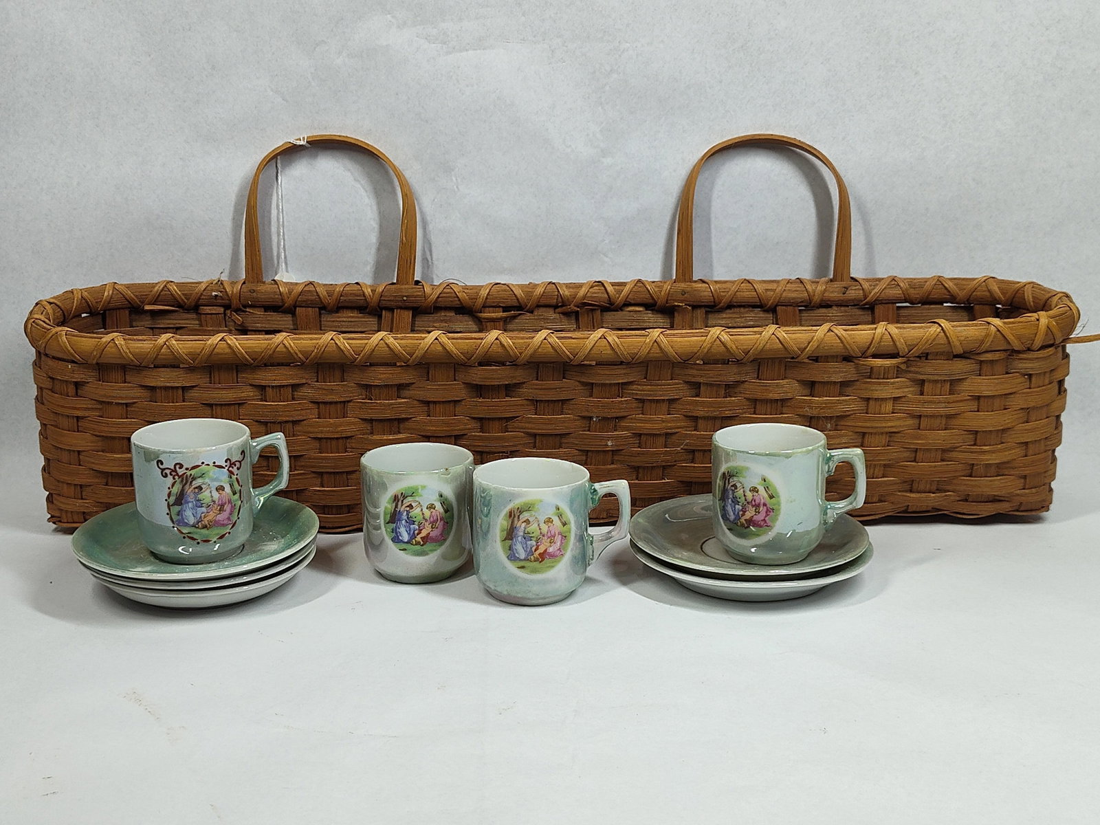 Japanese Lusterware Demitasse w/ Basket: A vintage Japanese demitasse set consisting of four ceramic cups and five saucers, presented in a long, rectangular woven wicker carrying basket with dual arched handles. The ceramic pieces are finish