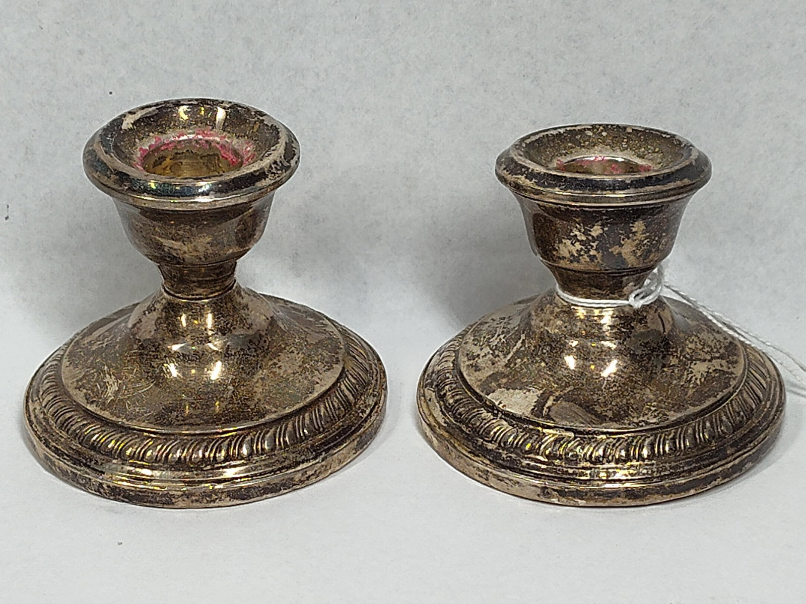 Pair Sterling Gadrooned Candlesticks: This pair of low candlesticks is designed in a classical revival style. Each piece features a short baluster-form stem rising from a wide, domed circular base. The shoulder of each base is decorated