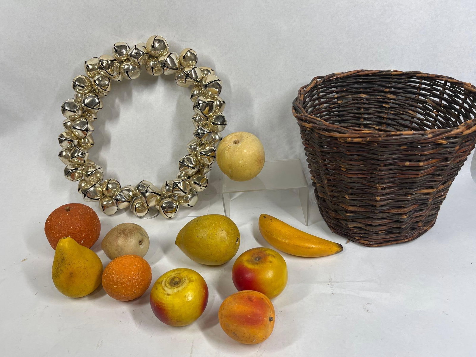 Bell Wreath, Basket & Artificial Fruit: This decorative grouping includes a holiday-themed jingle bell wreath, a rustic woven basket, and ten pieces of artificial fruit. The wreath is a large circular decoration composed of numerous