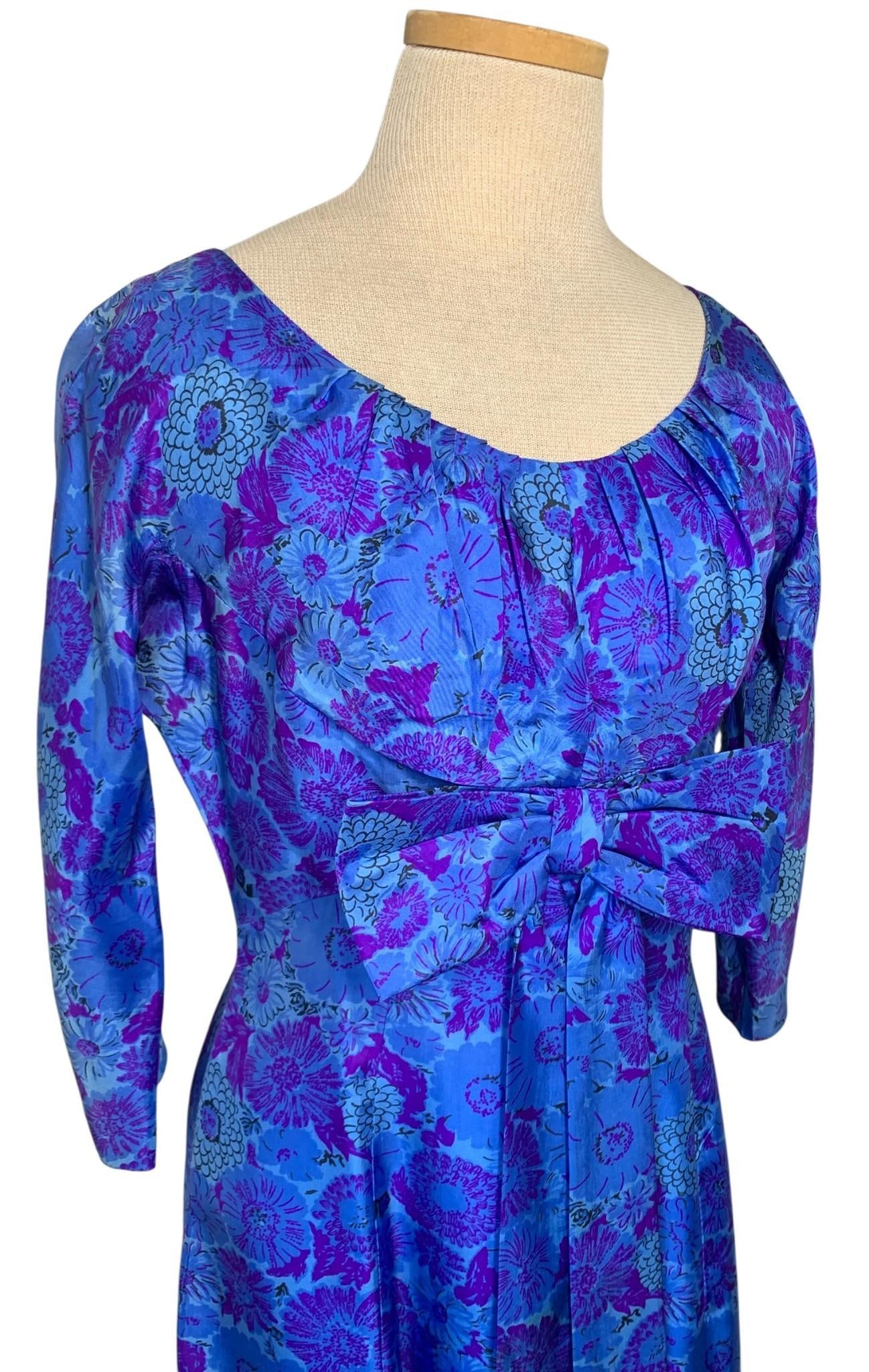 Luxe Mid Century Sapphire & Plum Floral Printed Silk Bow Trimmed Cocktail Dress: Iconic 60s styling with ruched bust, oversize self fabric bow and slim bracelet sleeve, working metal zipper, small area at the lower back with minor fade, no underarm issues, superb fabric in vivid h
