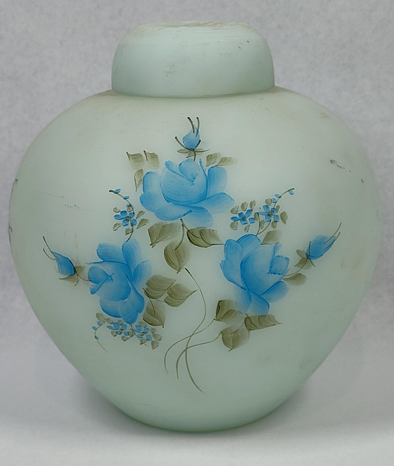 Fenton Blue Roses Blue Satin Ginger Jar: 6.5x6. A Fenton Art Glass ginger jar with a matching lid, crafted in blue satin frosted glass. The vessel features a bulbous body decorated with a hand-painted floral motif known as Blue Roses on