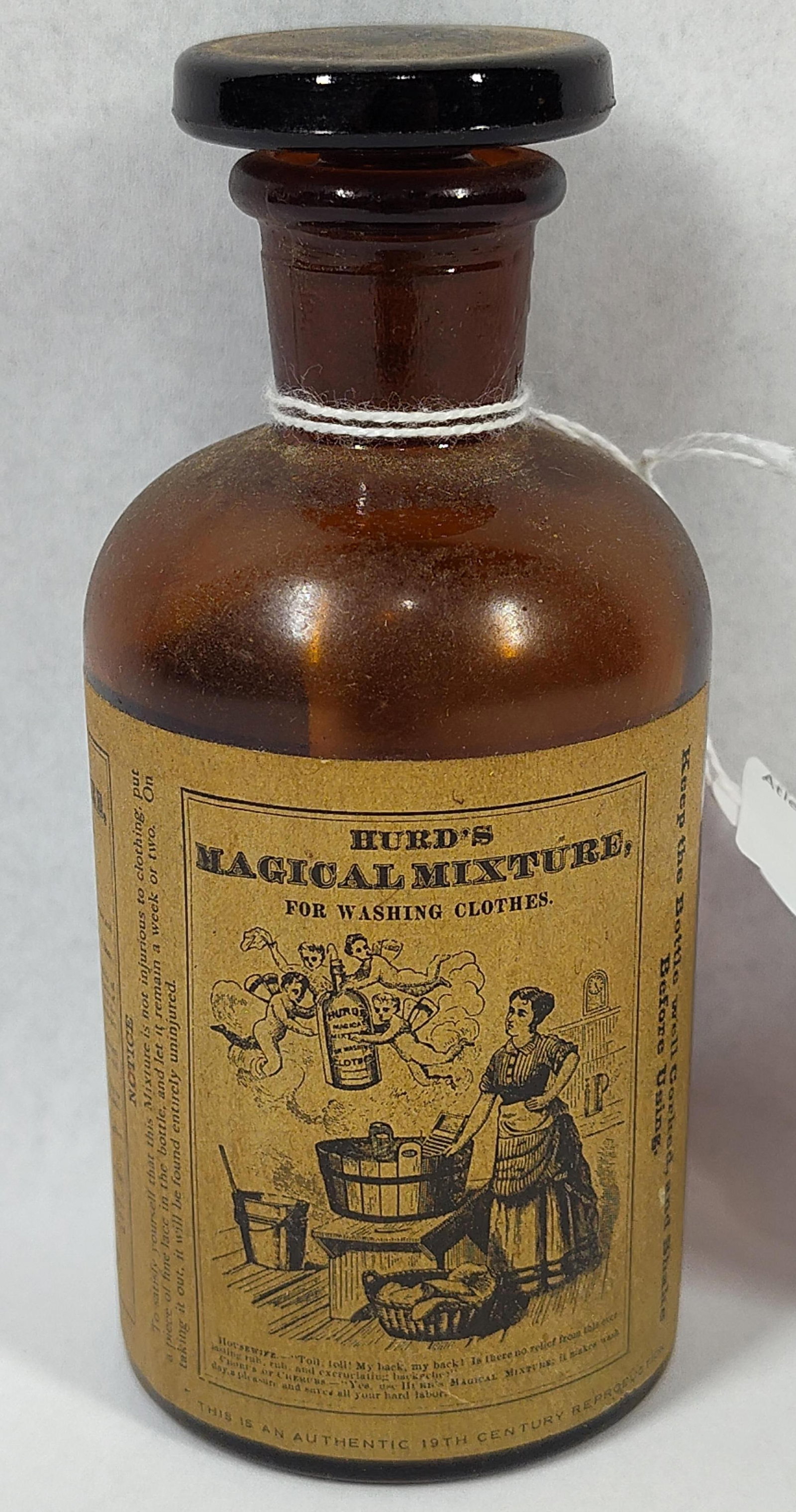 14) (15) H(20) (21) M(28) (29) M(36): 5 inches.This amber glass bottle with a black glass stopper is a late 20th-century reproduction of a 19th-century advertising bottle. It features a large, wrap-around paper label for Hurds Magical