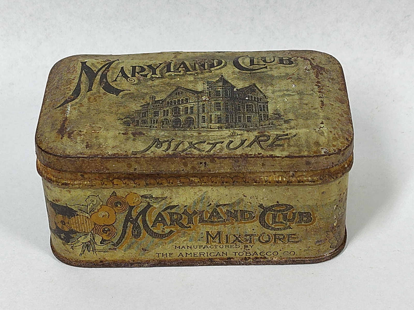 American Tobacco Maryland Club Tin: 4x1.5x2.5 Antique lithographed metal tobacco tin for Maryland Club Mixture pipe tobacco. This pocket-sized tin features a hinged lid and decorative graphics on all exterior sides. The lid displays a