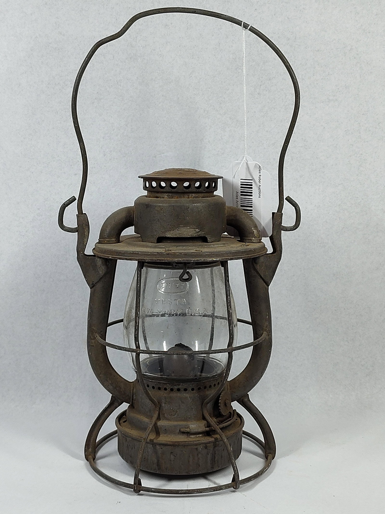 Dietz Vesta NY Central Railroad Lantern: 10 in. An antique Dietz Vesta railroad lantern featuring a metal frame and clear glass globe. The top chimney cap is embossed with the Dietz Vesta logo inside an oval. The upper horizontal rim of the