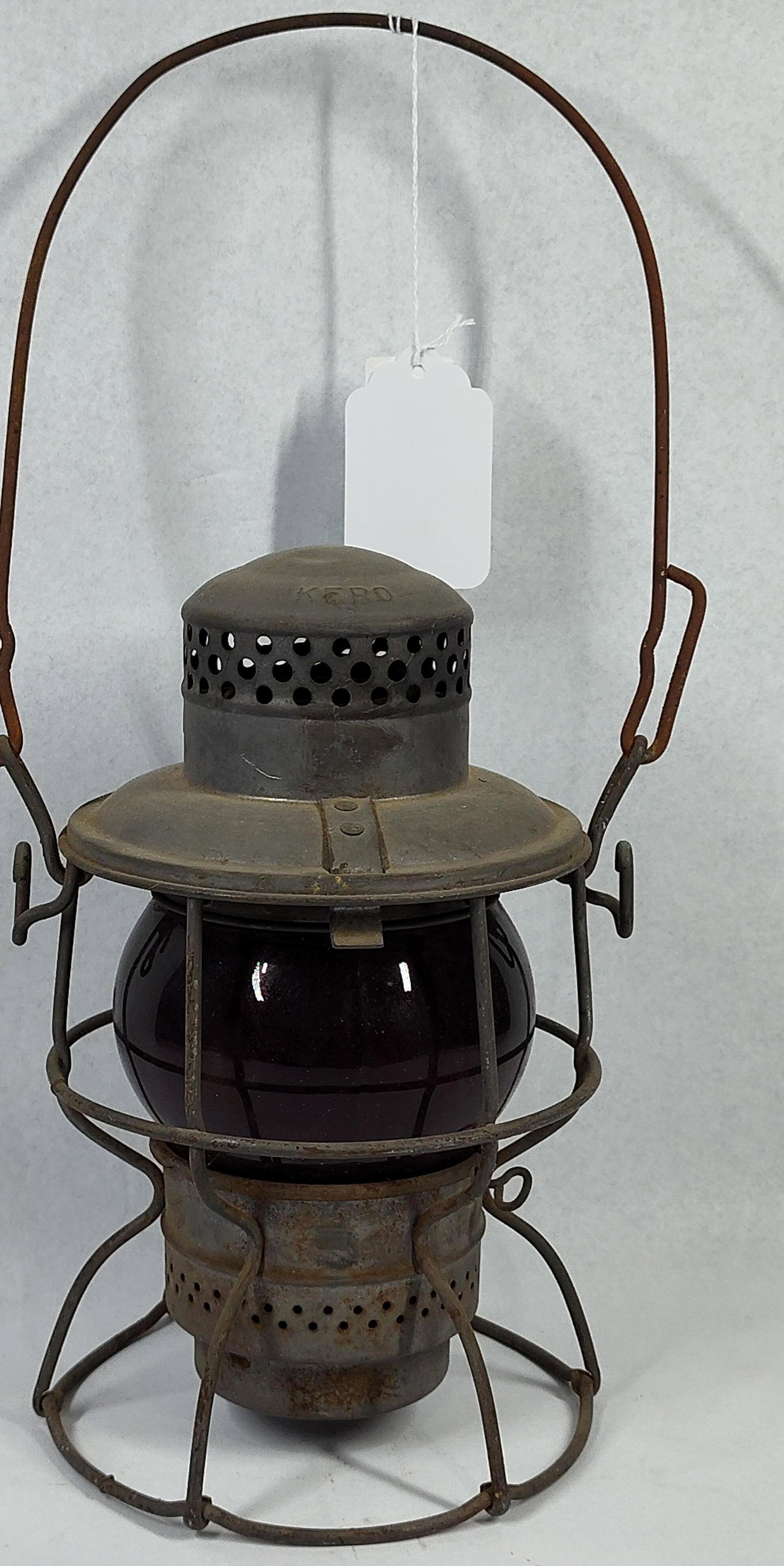 Adlake Kero Railroad Red Globe Lantern: 10 in. This is an Adlake Kero short-globe railroad lantern produced by Adams & Westlake. The lantern is constructed with a metal frame and chimney featuring a dark, aged patina. The top of the