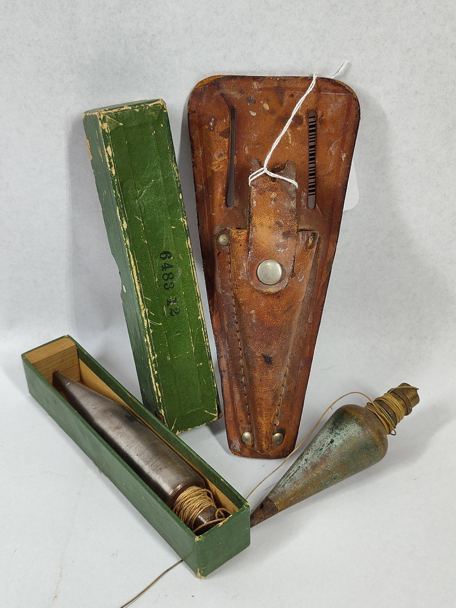 Pair Vtg Surveyor Plumb Bobs w/ Box: This lot features two vintage surveyor plumb bobs, one storage box, and a leather belt holster, typical of mid-20th-century industrial equipment. The first plumb bob is constructed of steel with a
