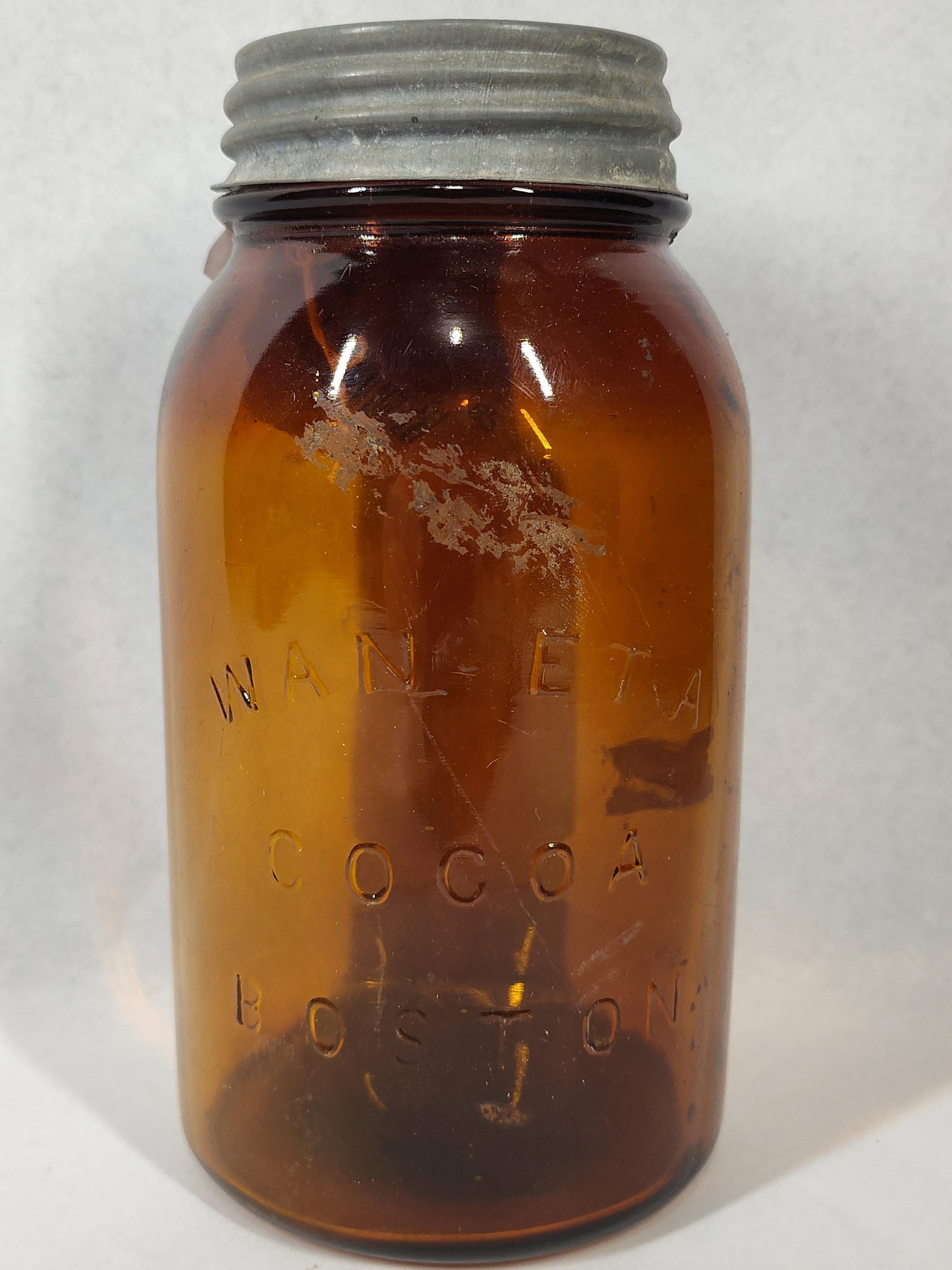 Wan-Eta Cocoa Amber Advertising Jar: An antique amber glass advertising jar produced for the Wan-Eta Cocoa Company of Boston, Massachusetts. The jar features a cylindrical form with a tapered shoulder and a threaded neck. The front is
