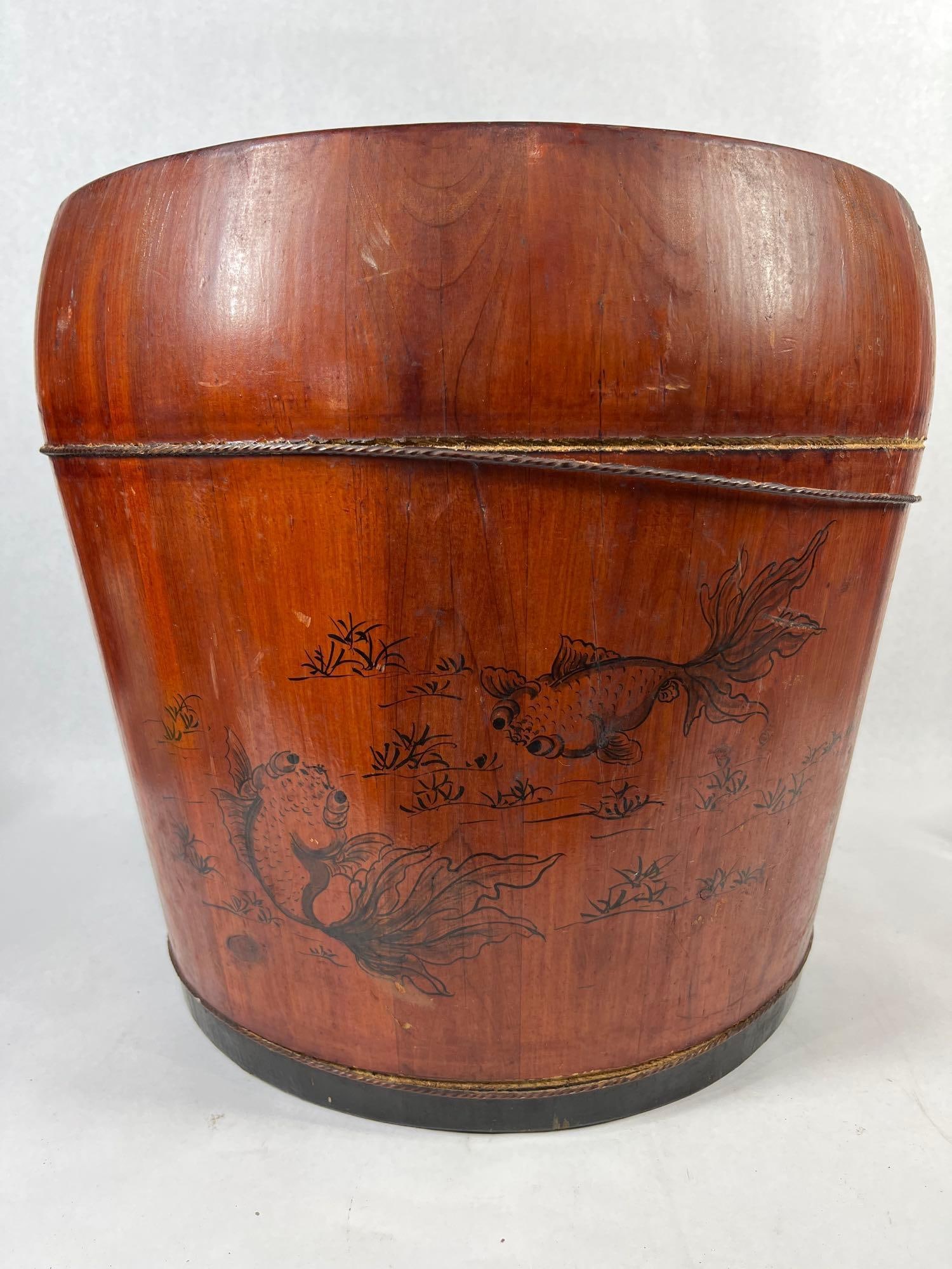 Chinese Red Lacquered Goldfish Bucket: 14X14.5 A Chinese wooden bucket or pail with a fixed, arched overhead handle. The exterior is finished with a reddish-brown lacquer or stain. The body is bound with two thin wire hoops. The side of th