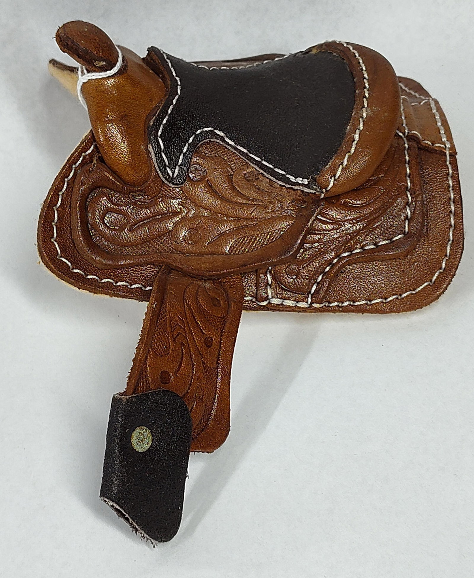 Miniature Western Decorative Saddle: 4.5x4. Miniature scale decorative Western saddle. The item features brown leather construction with embossed floral and leaf tooling on the skirts and fenders. The seat is finished in a contrasting