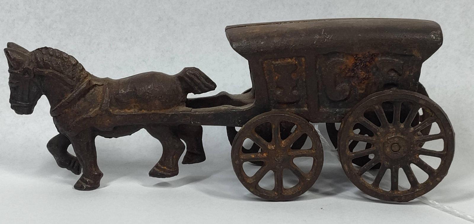 Kenton or Williams Ice Wagon Still Bank: 8 inches. This horse-drawn ice delivery wagon still bank is constructed of cast iron. The wagon features a two-part body joined at a central seam, which includes a coin slot integrated into the