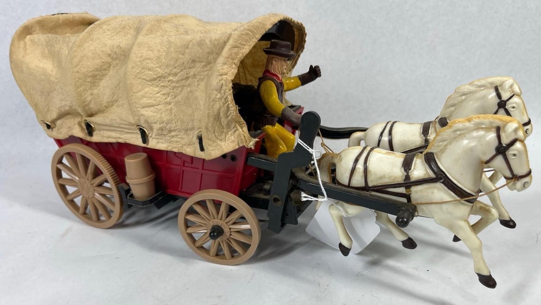 Wild West Wagon w/ Driver & Pair Horses: 15 in long. A vintage battery-operated Wild West covered wagon toy, constructed primarily of molded plastic. The wagon features a red body mounted on a black chassis with tan spoked wheels. The rear