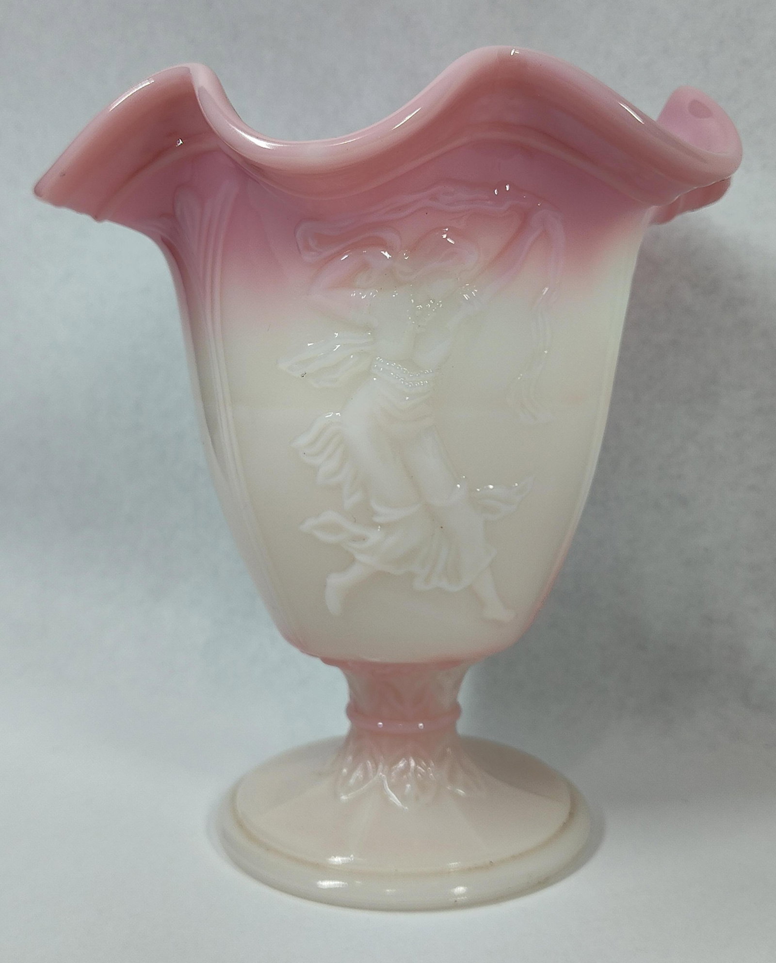 Fenton Rosalene Dancing Ladies Vase: This footed art glass vase is crafted from Rosalene glass, a heat-sensitive opaque material that transitions from a rose-pink ruffled rim to a creamy-white base. The body is decorated with the