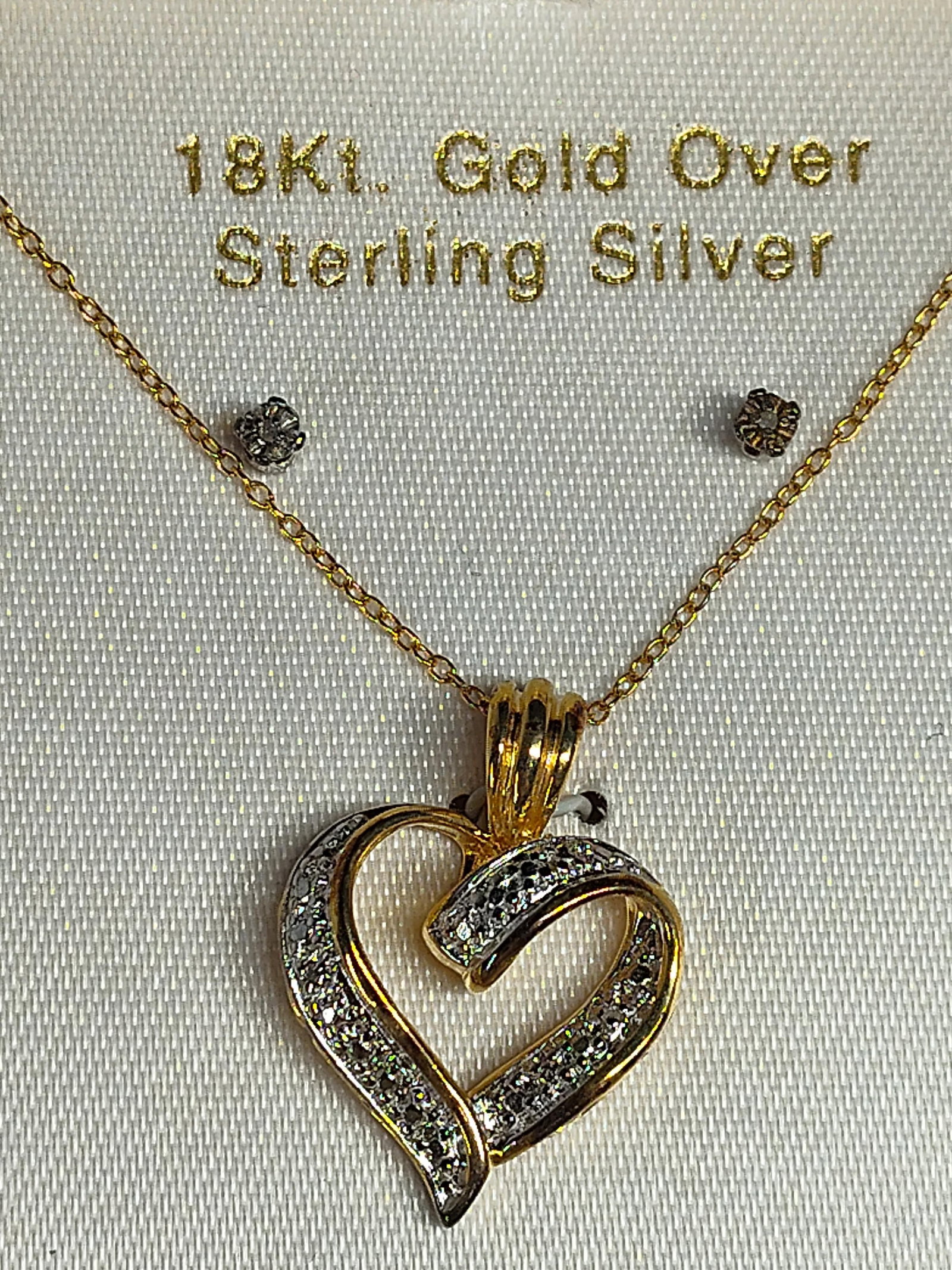 Diamond 18K Gold/Str. Heart Jewelry Set: This jewelry set includes a pendant necklace and matching stud earrings. The pendant is designed as an open heart in a yellow gold tone with a decorative ribbon crossover. Small round diamond accents 