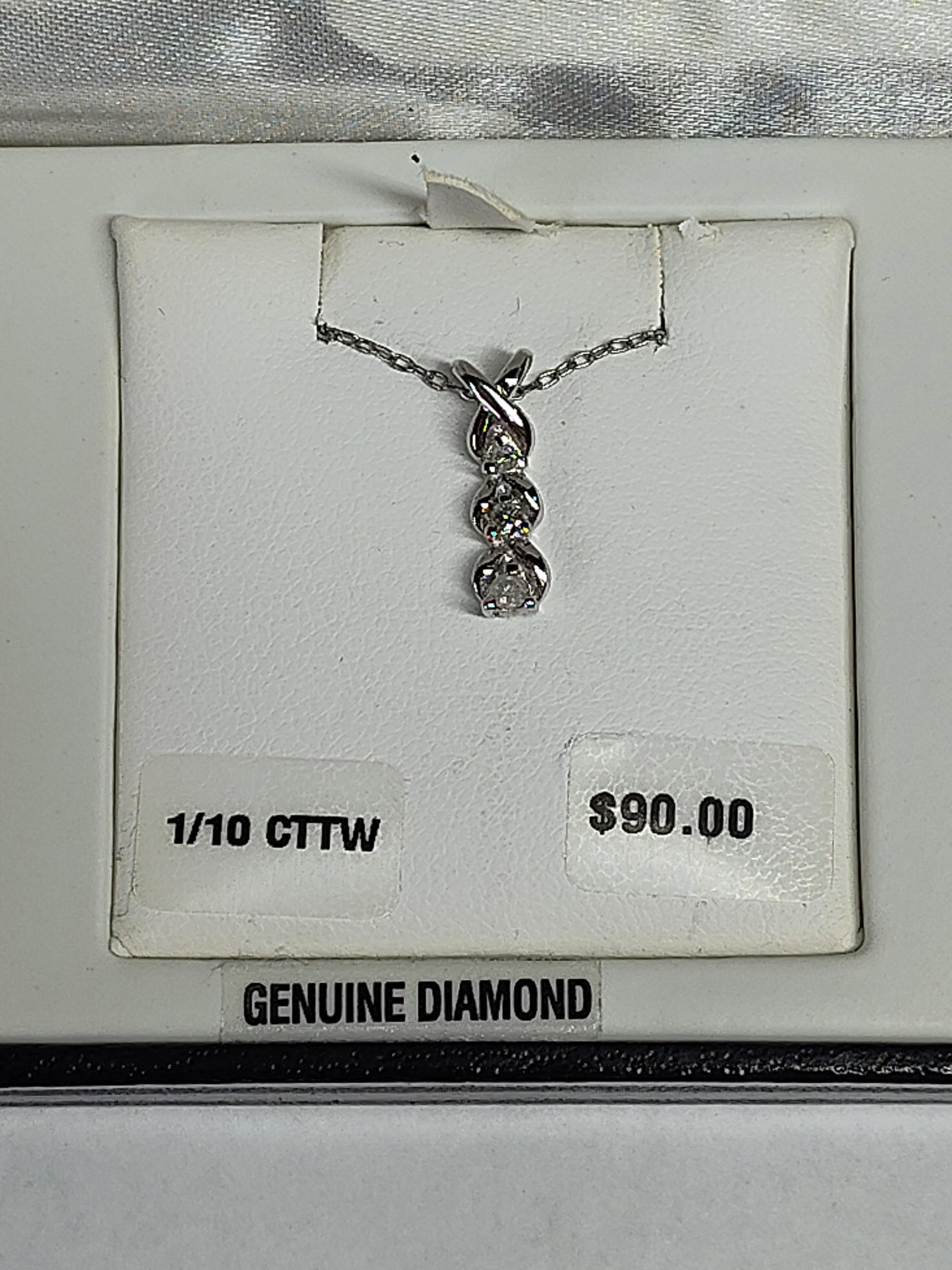 Diamond Three-Stone Pendant Necklace: A linear three-stone diamond pendant necklace presented in its original retail packaging. The pendant features three small round-cut diamonds arranged in a vertical drop, each held in a white metal se