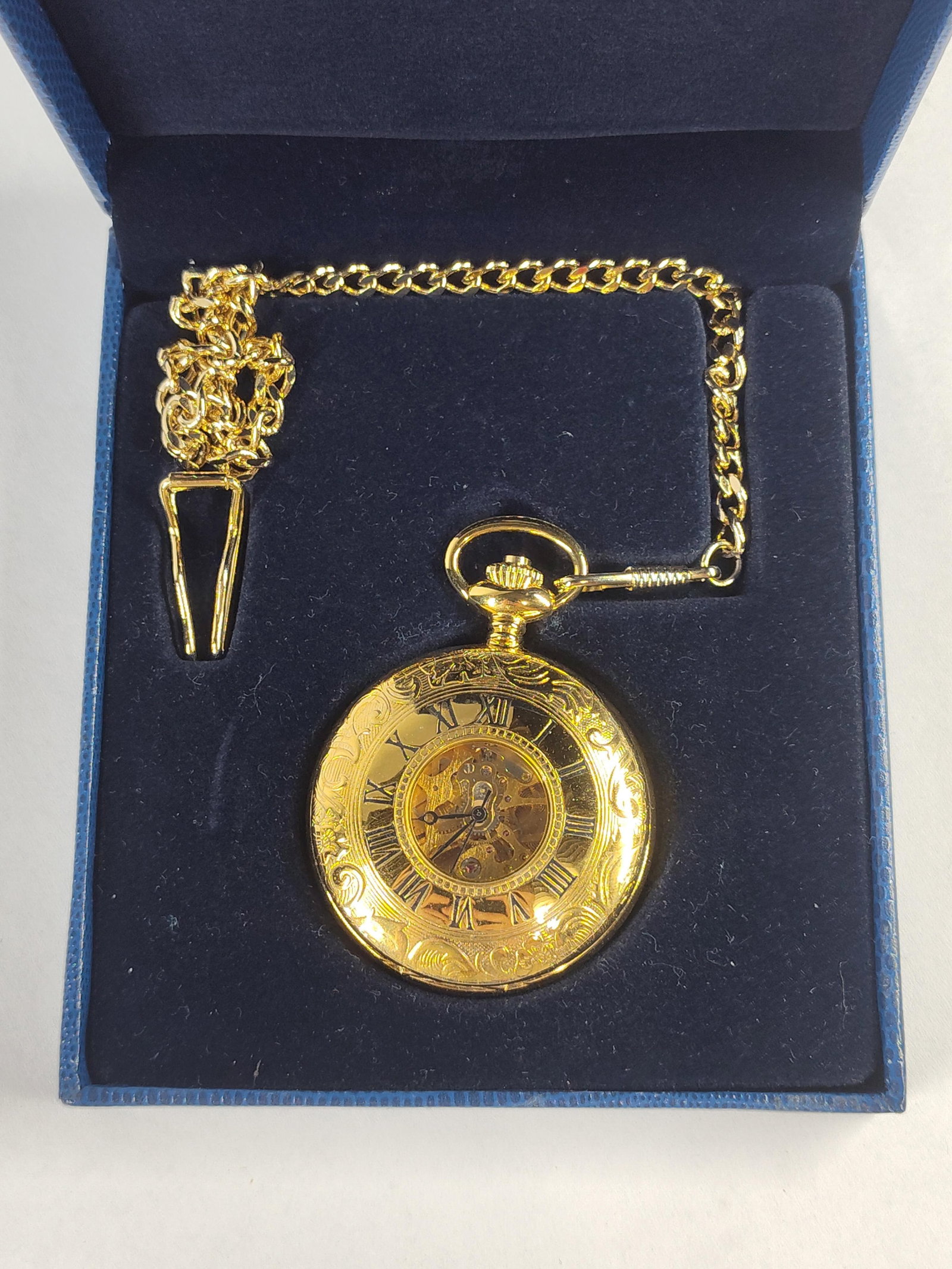 Charles-Hubert Skeleton Pocket Watch: A contemporary manual-wind pocket watch produced by Charles-Hubert, Paris. The timepiece features a gold-plated hunter-style case decorated with intricate foliate scroll engravings on both the front