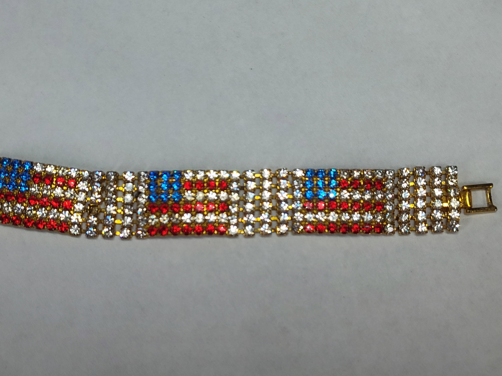 Oriental Trading Americana Flag: A wide, five-row flexible costume jewelry bracelet featuring a repeating patriotic American flag motif. The design incorporates five individual flag sections rendered in red, blue, and clear faceted