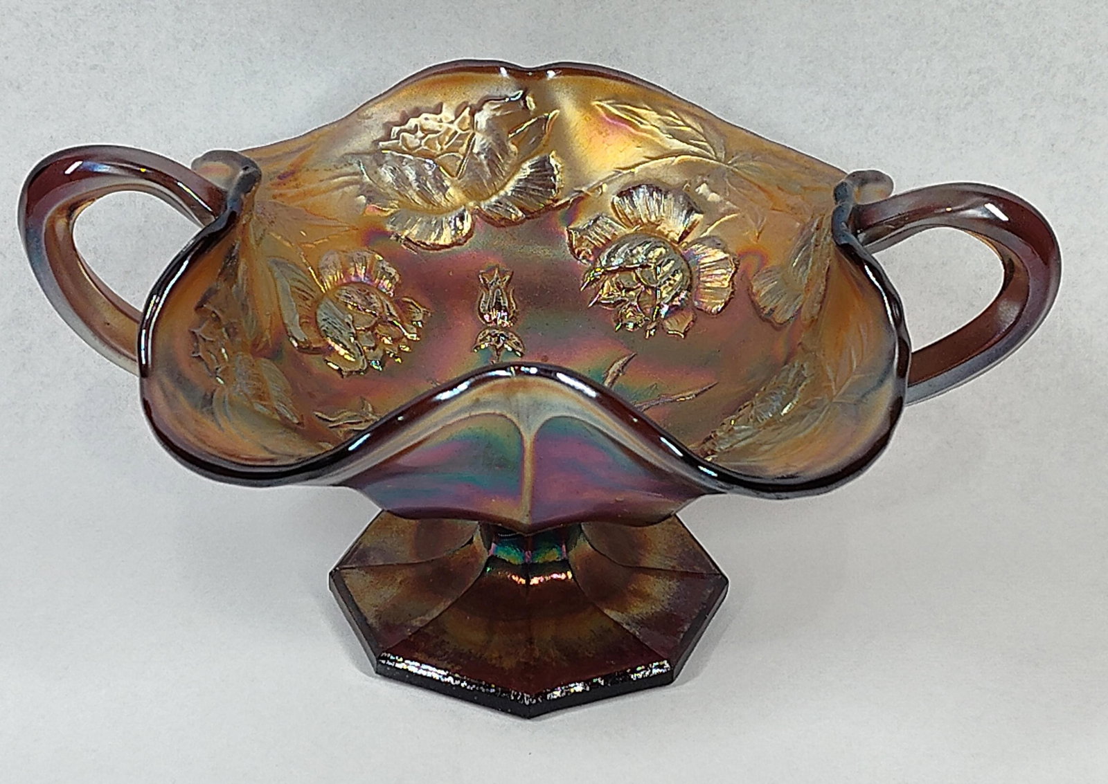 Attr Fenton Amethyst Carnival Bonbon: This is a footed, two-handled bonbon dish in the Wreath of Roses pattern, attributed to the Fenton Glass Company, United States, circa 1910-1920. The item is made of pressed amethyst glass with a