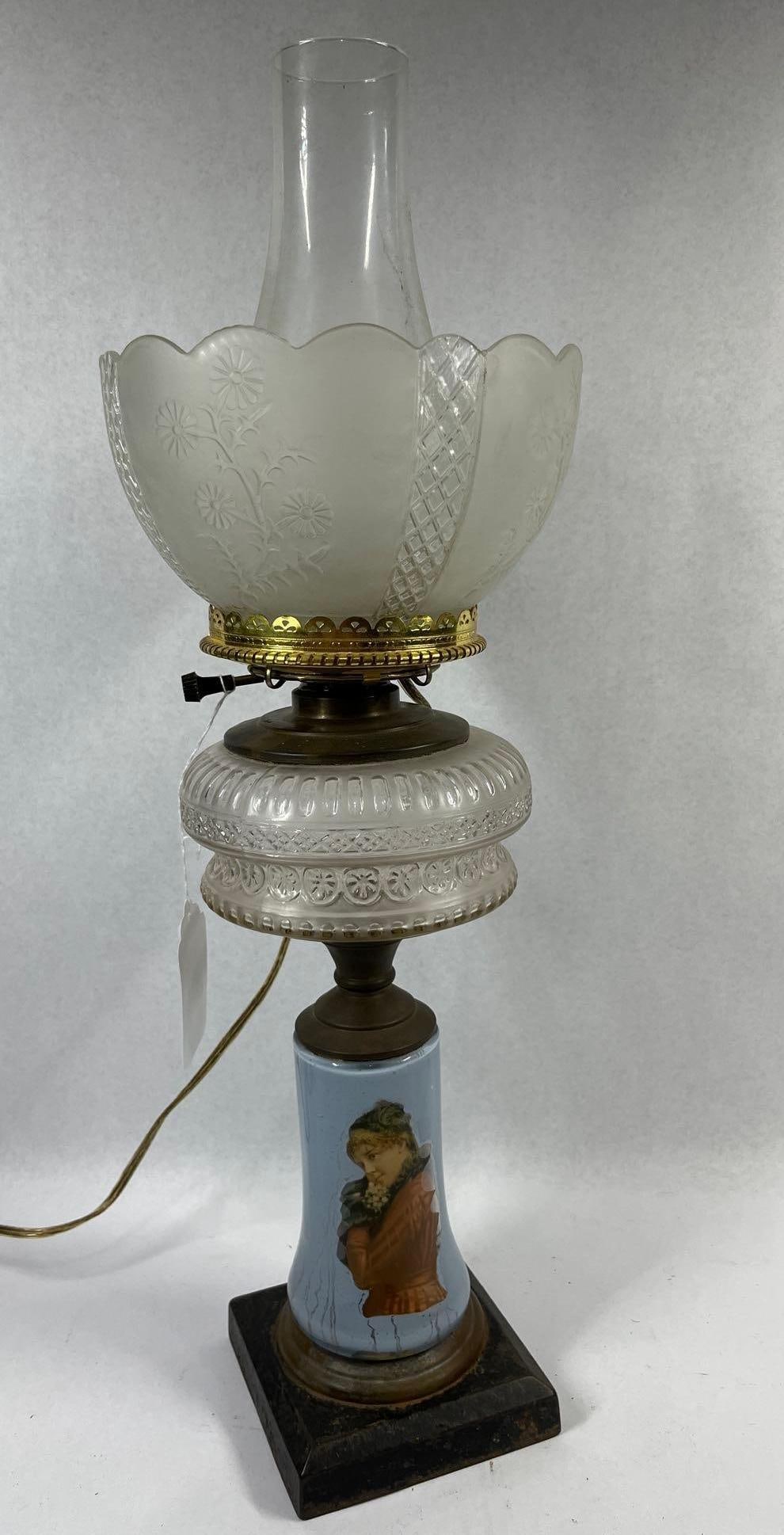 Victorian Style Portrait Kerosene Lamp: 22 in tall. This is an electrified Victorian-style kerosene table lamp featuring mixed-material construction. The lamp stands on a square, dark-finished cast metal plinth base, likely iron. The pedest