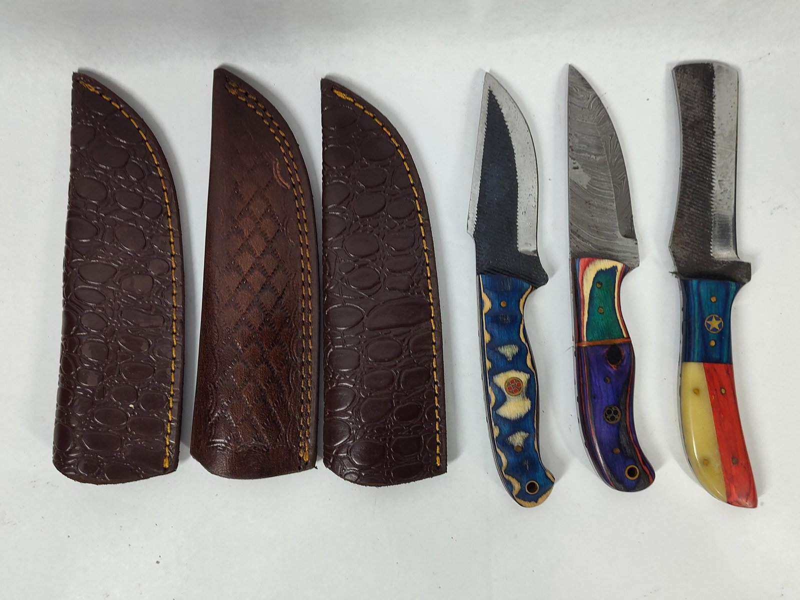 3 Custom Fixed-Blade Knives w/ Sheaths: 4 in blades. 8 in handles. This lot consists of three custom fixed-blade knives of varying styles, each with its own leather sheath. The first knife is a skinner/utility design with a blade