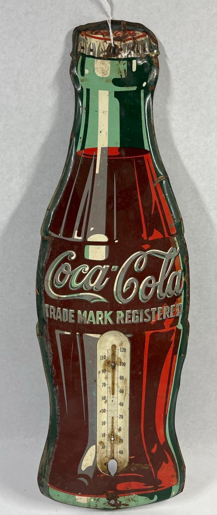 Coca-Cola Metal Bottle Thermometer Sign: 17.5 in. No mercury. A vintage advertising thermometer sign produced for Coca-Cola, constructed of die-cut lithographed sheet metal. The sign is shaped in the likeness of the brand's iconic contou