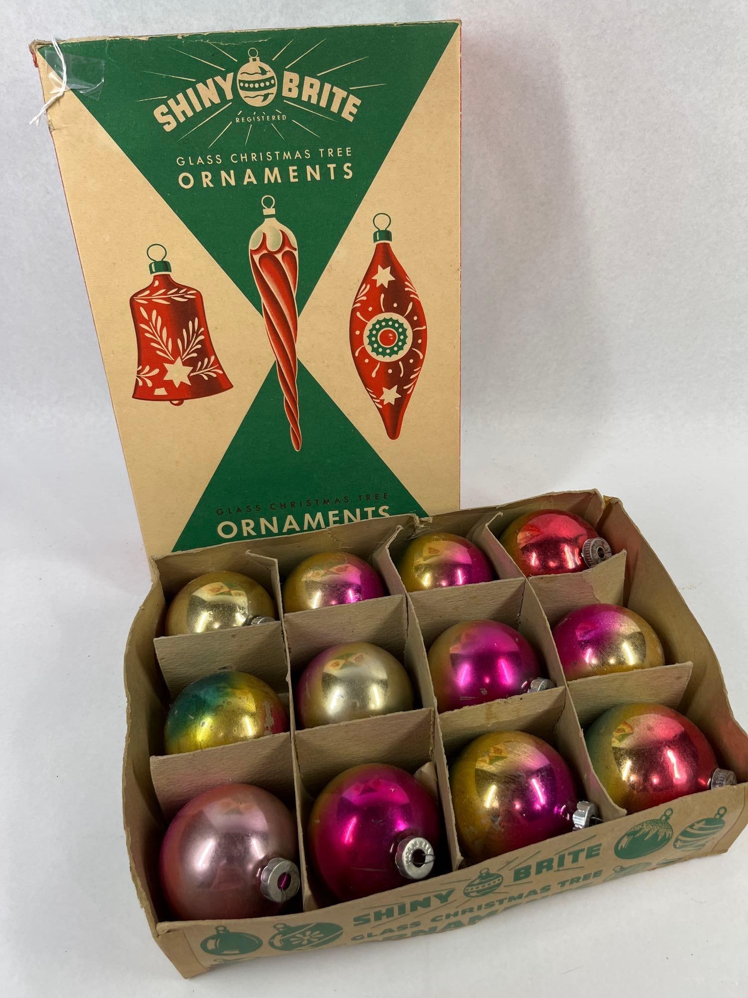 Set Vtg Shiny Brite Glass Ornaments Box: A collection of spherical glass Christmas tree ornaments presented in an original Shiny Brite cardboard box. The ornaments are constructed of blown glass with silvered interiors and feature a variety