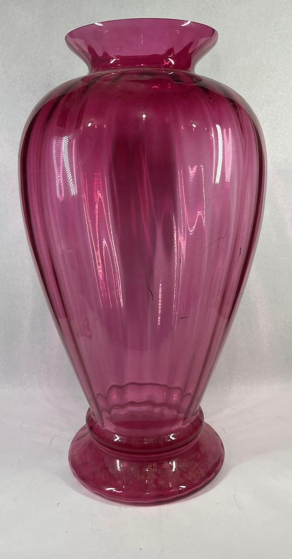 Cranberry Glass Optic Rib Pedestal Vase: 30 in tall. Attributed to Pilgrim Glass, this large pedestal vase is constructed from translucent cranberry glass, characterized by its deep magenta hue. The piece features a tapering ovoid form with