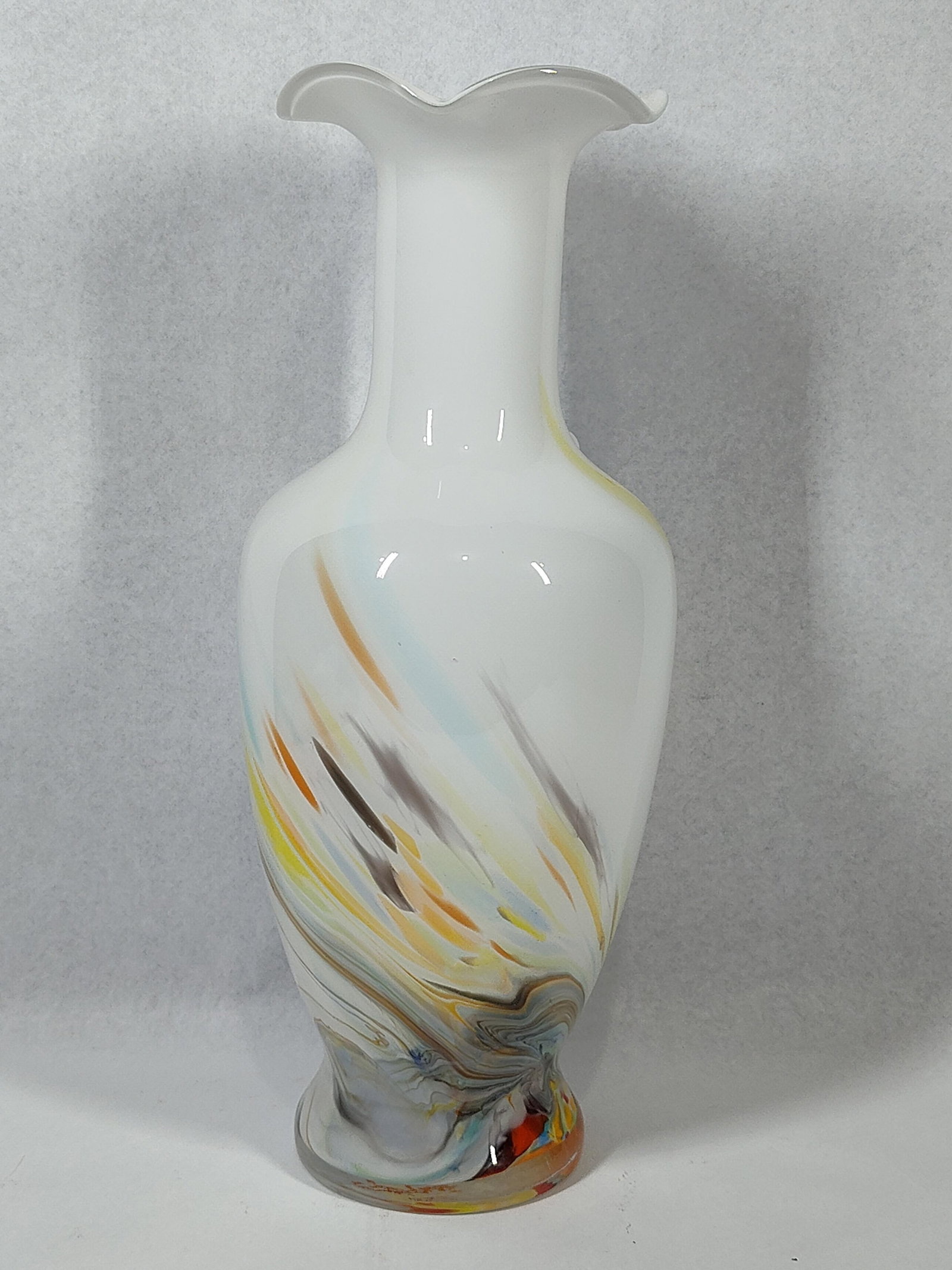 Hand-Blown White Glass Color Swirl Vase: 14 inches. A hand-blown art glass vase featuring an opaque white cased body decorated with multi-colored swirls. The lower half of the vessel displays integrated streaks of yellow, orange, blue,