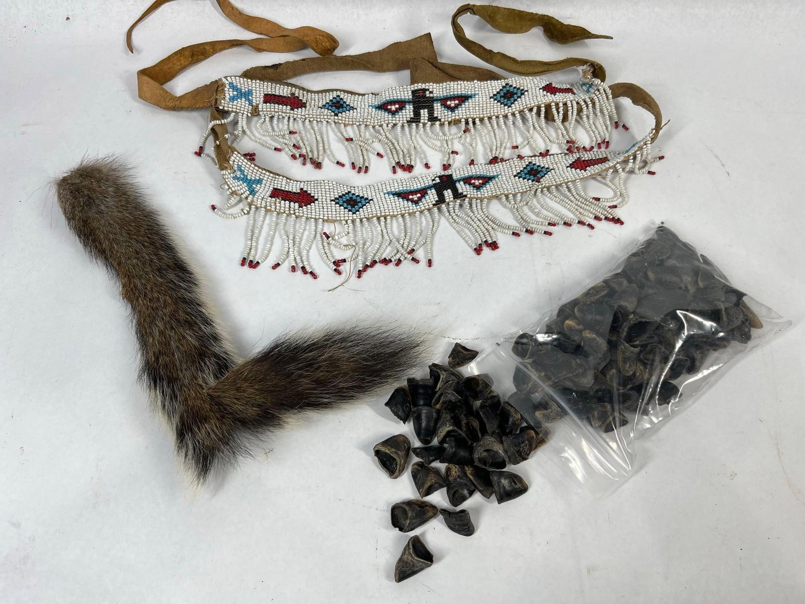Indigenous Style Beaded & Hide Regalia: A group of North American Indigenous style regalia and craft components. The lot features a beaded hide band or sash, a fur animal tail, and an assortment of small animal hooves. The beaded band is